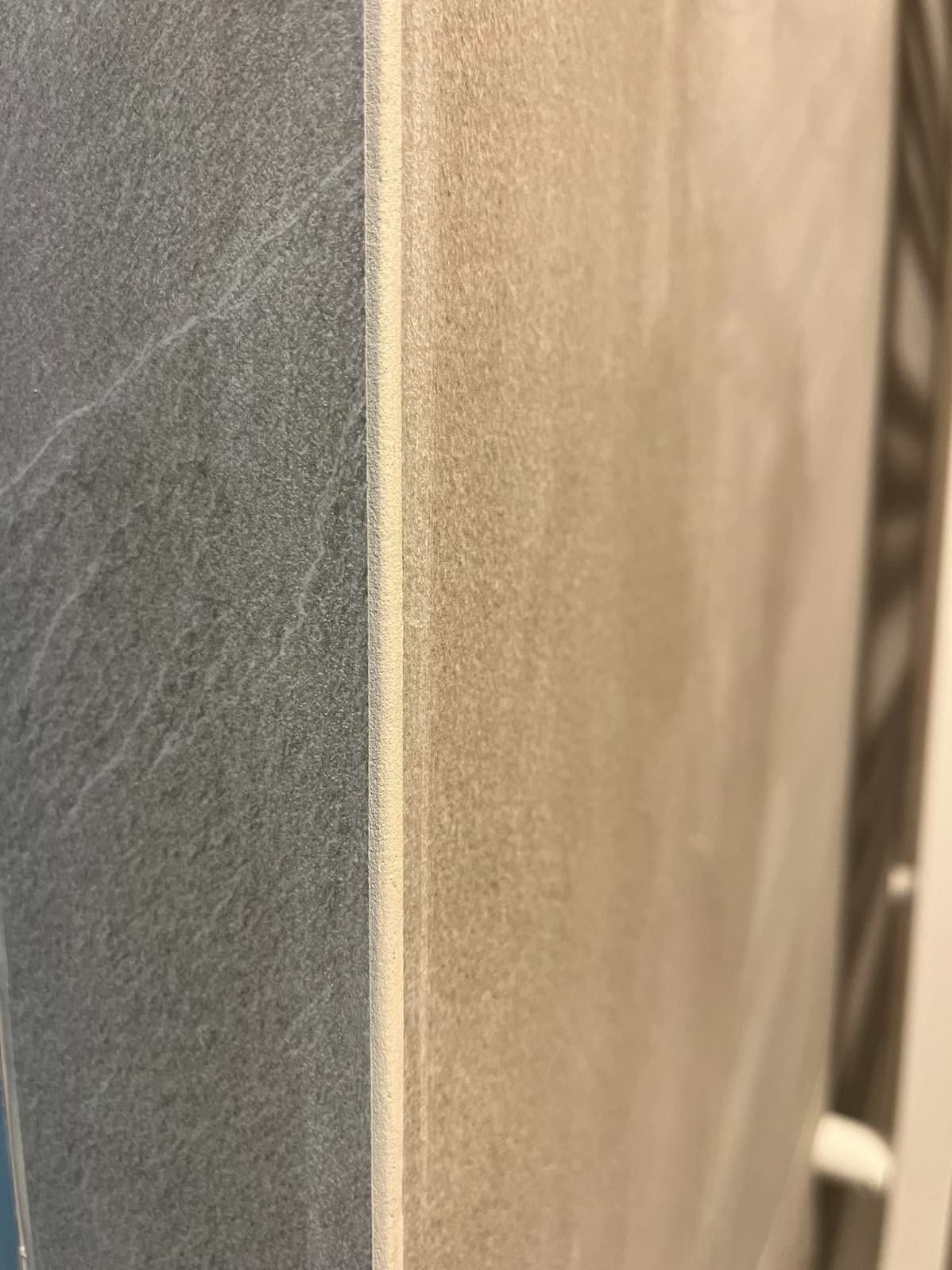 Szczegółowe zbliżenie na połączenie płytek w łazience: szara płytka imitująca kamień sąsiaduje z beżową, z widoczną fugą.