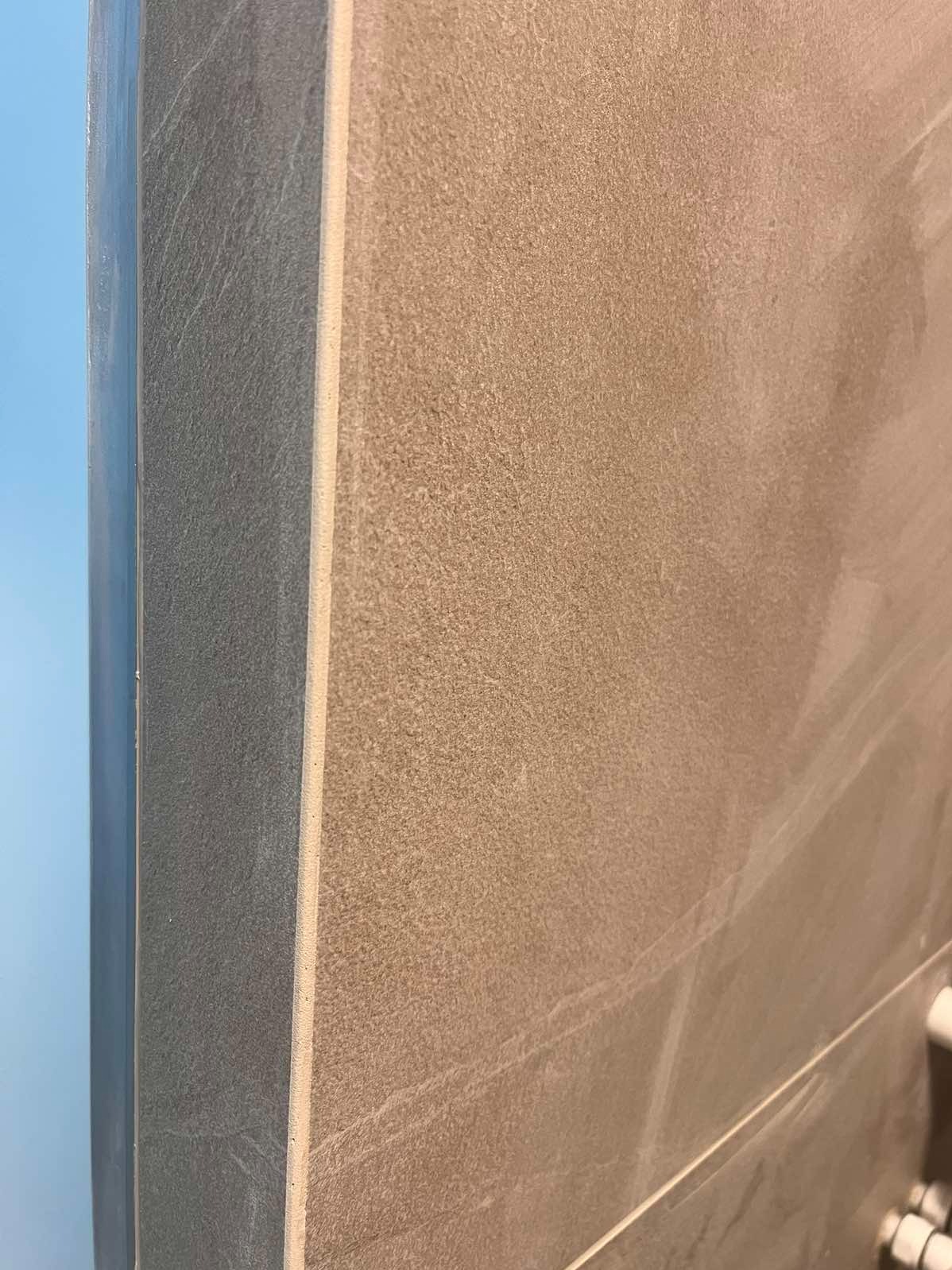 Detal wykończenia ściany z beżowych płytek, widoczny narożnik i fuga. Minimalistyczny design, neutralna kolorystyka, ciepłe oświetlenie.