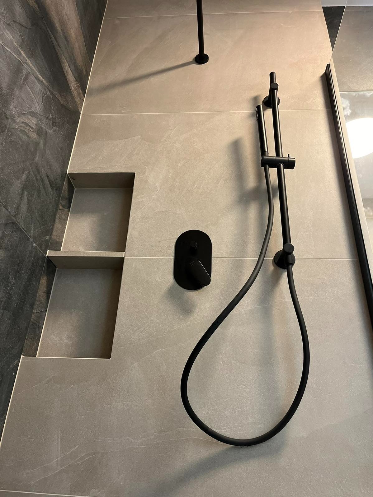 Nowoczesna kabina prysznicowa z czarną armaturą i wnękami w jasnych płytkach, wykończona szarą okładziną. Minimalistyczny design.