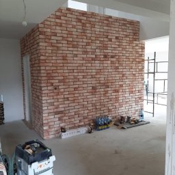 MarcusKowal1989 - Ceglana ściana dekoracyjna w surowym wnętrzu. Widoczne narzędzia i materiały budowlane. Ściana z cegły tworzy oddzielną przestrzeń w pomieszczeniu.