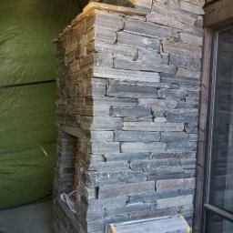 MarcusKowal1989 - Kamienny kominek w trakcie budowy, z widoczną drabinką i zieloną plandeką w tle. Detal wykończenia wnętrza z naturalnego kamienia.