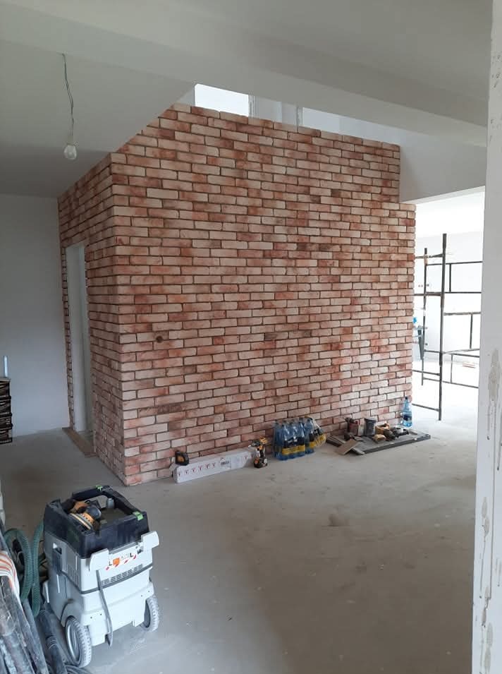 Ceglana ściana dekoracyjna w surowym wnętrzu. Widoczne narzędzia i materiały budowlane. Ściana z cegły tworzy oddzielną przestrzeń w pomieszczeniu.