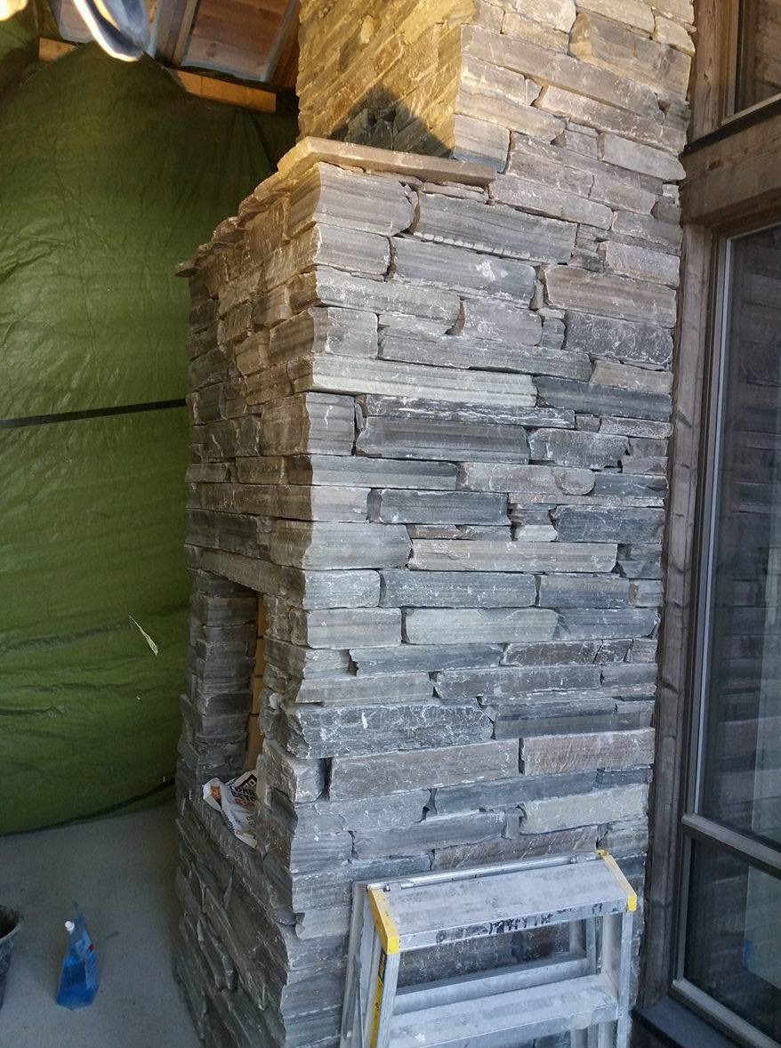 Kamienny kominek w trakcie budowy, z widoczną drabinką i zieloną plandeką w tle. Detal wykończenia wnętrza z naturalnego kamienia.