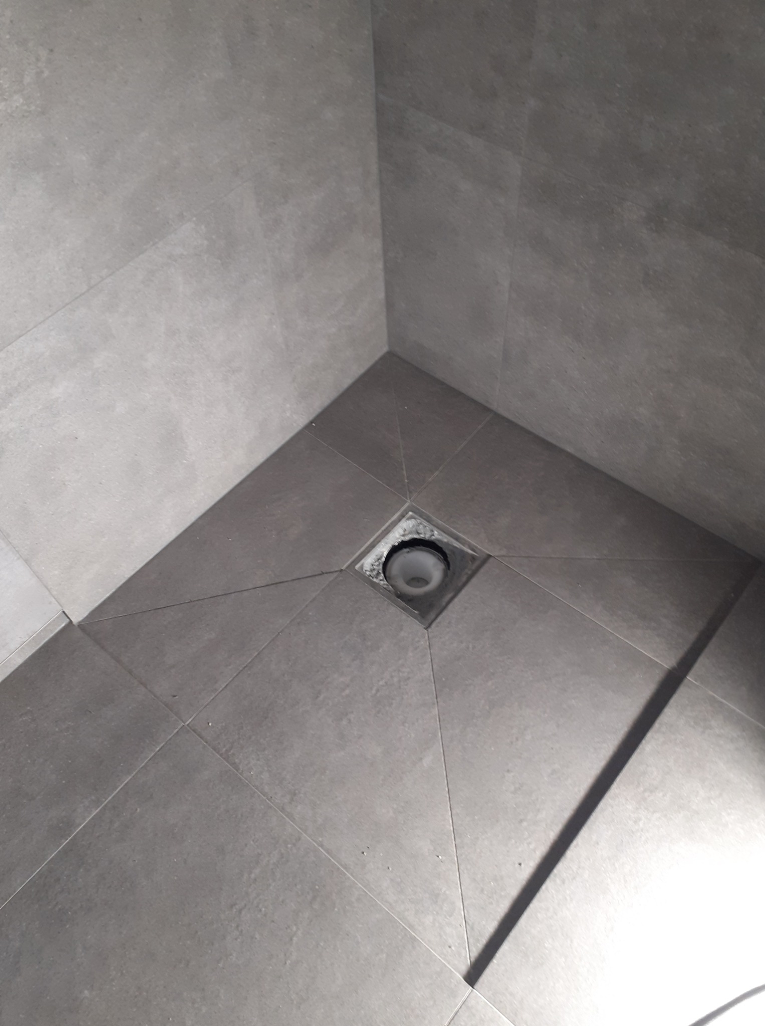 Szare, matowe płytki w kabinie prysznicowej z odpływem liniowym. Minimalistyczny design, oświetlenie podkreśla fakturę płytek. Wykończenie z dbałością o detale.