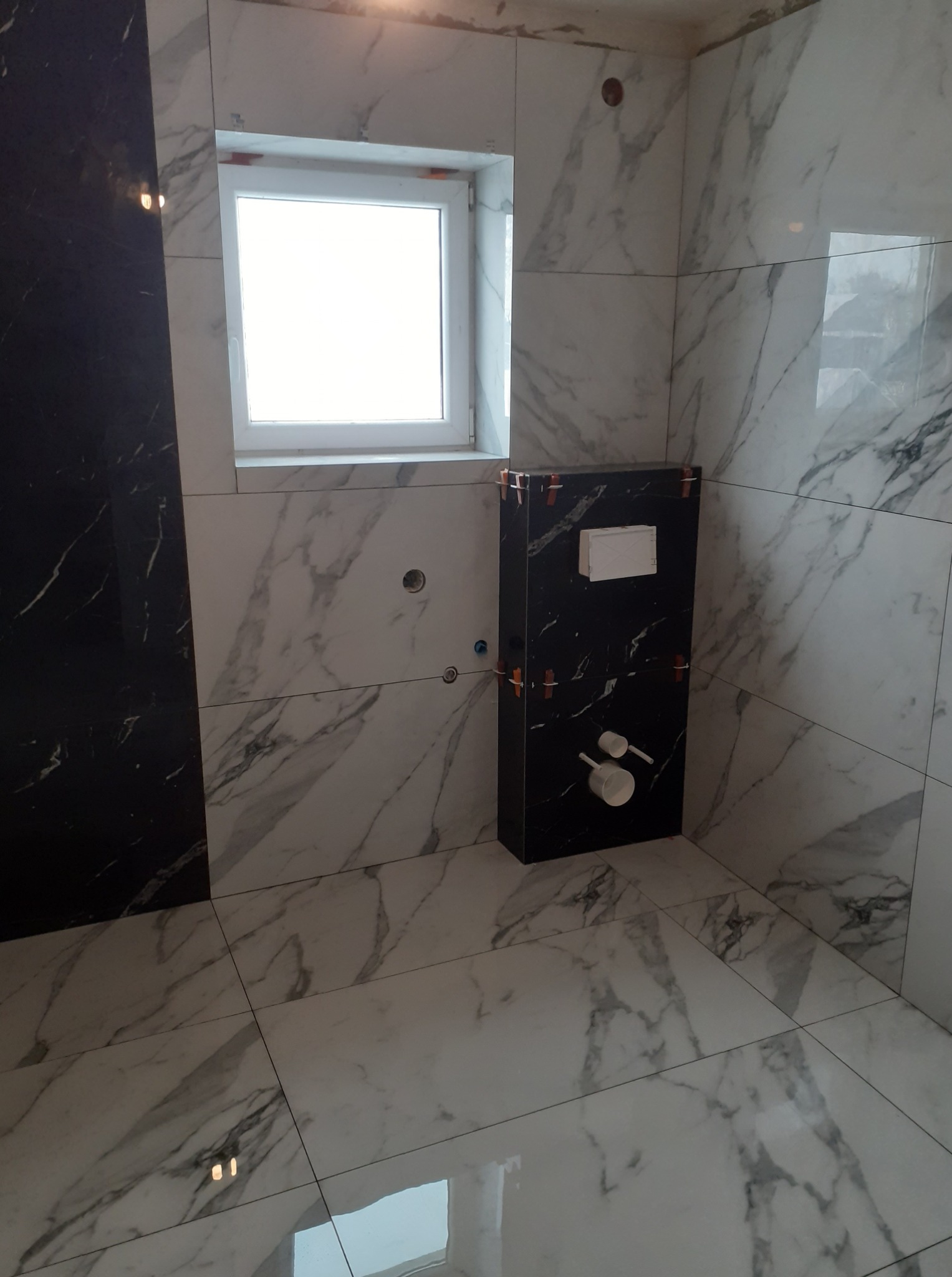 Łazienka w Jurkowie po remoncie: białe i czarne płytki imitujące marmur na ścianach i podłodze. Widoczna zabudowa podtynkowego WC w trakcie montażu.