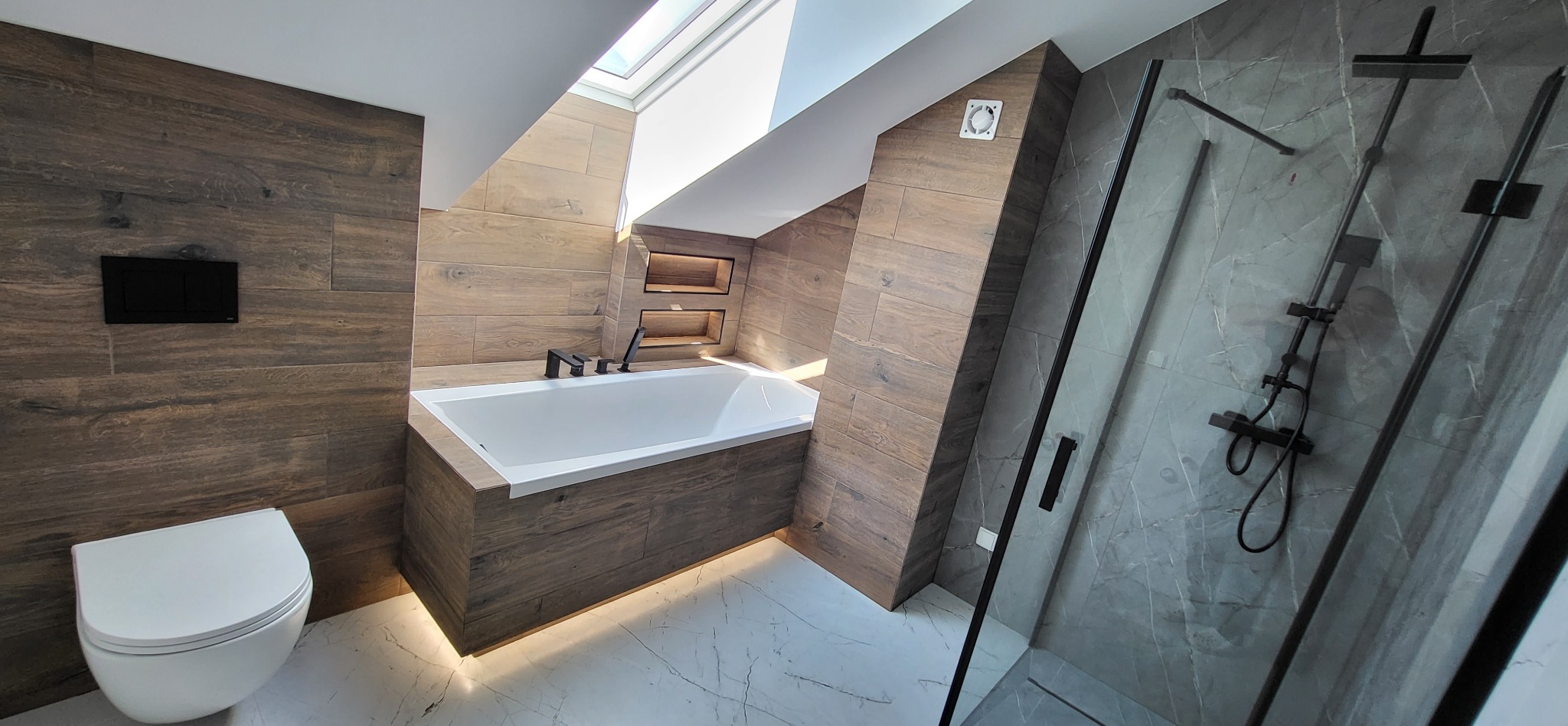 Nowoczesna łazienka na poddaszu: drewnopodobne płytki, wanna z podświetleniem LED, kabina prysznicowa z czarnym osprzętem, marmurowa podłoga i okno dachowe.