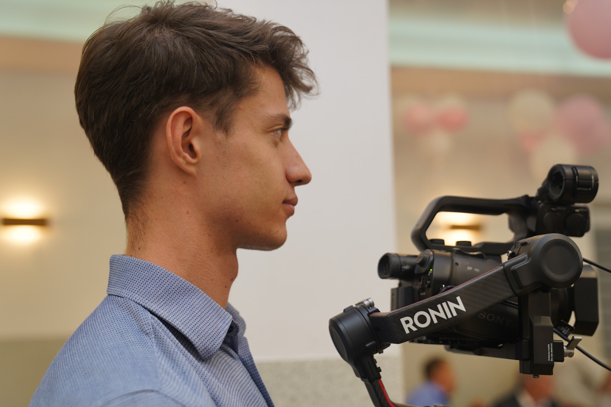 Profil mężczyzny z profesjonalną kamerą Ronin Sony, prawdopodobnie podczas filmowania wydarzenia z balonami w tle. Oświetlenie studyjne.