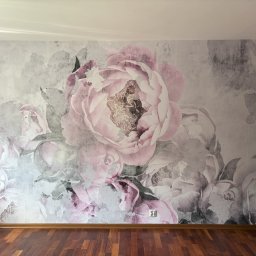 ABInterior - Ściana z fototapetą w kwiaty piwonii w odcieniach różu i szarości, widoczny fragment drewnianej podłogi i otwarte, drewniane drzwi.