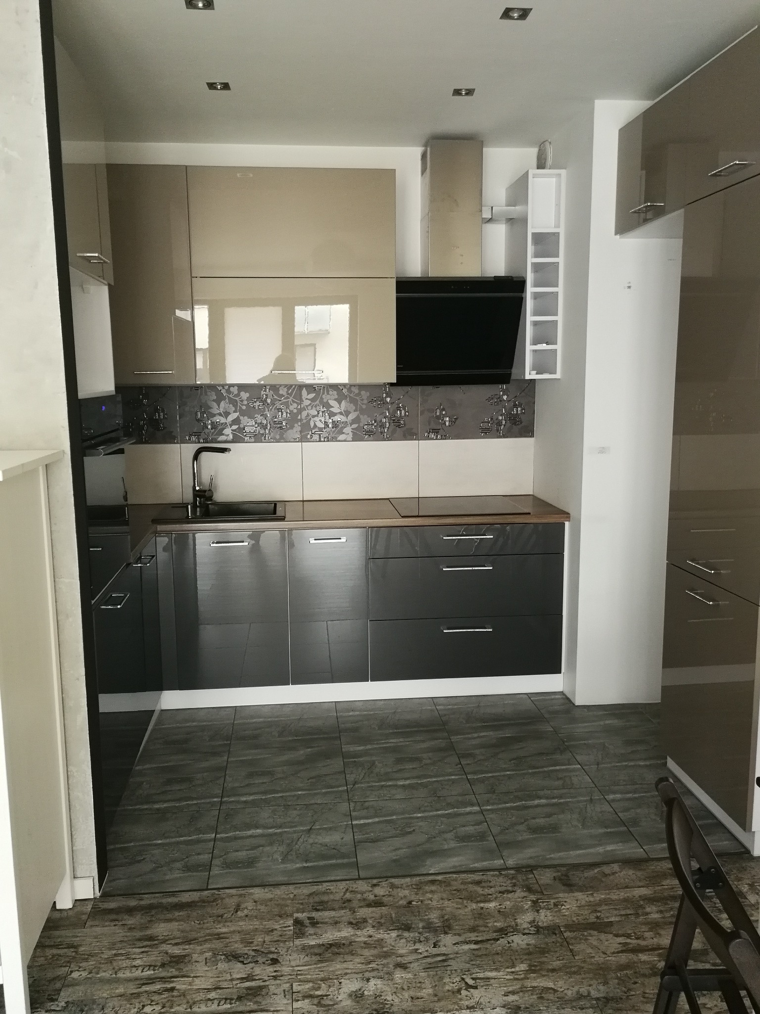 Nowoczesna kuchnia z połyskiem we Wrocławiu: szare szafki dolne, beżowe górne, dekoracyjne płytki nad blatem i ciemna podłoga. Minimalistyczny design.