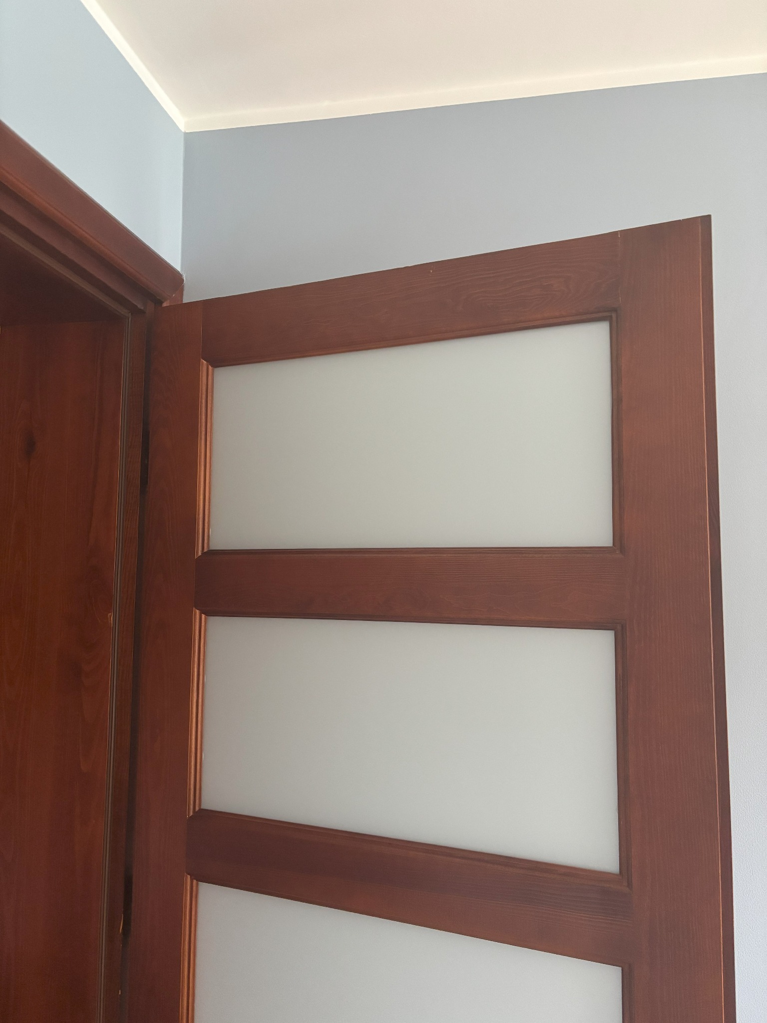 Otwarta, drewniana, trzyskrzydłowa  ościeżnica z matowym szkłem,  w jasnym wnętrzu z błękitnymi ścianami i białym sufitem. Widoczny fragment drugiej ościeżnicy.