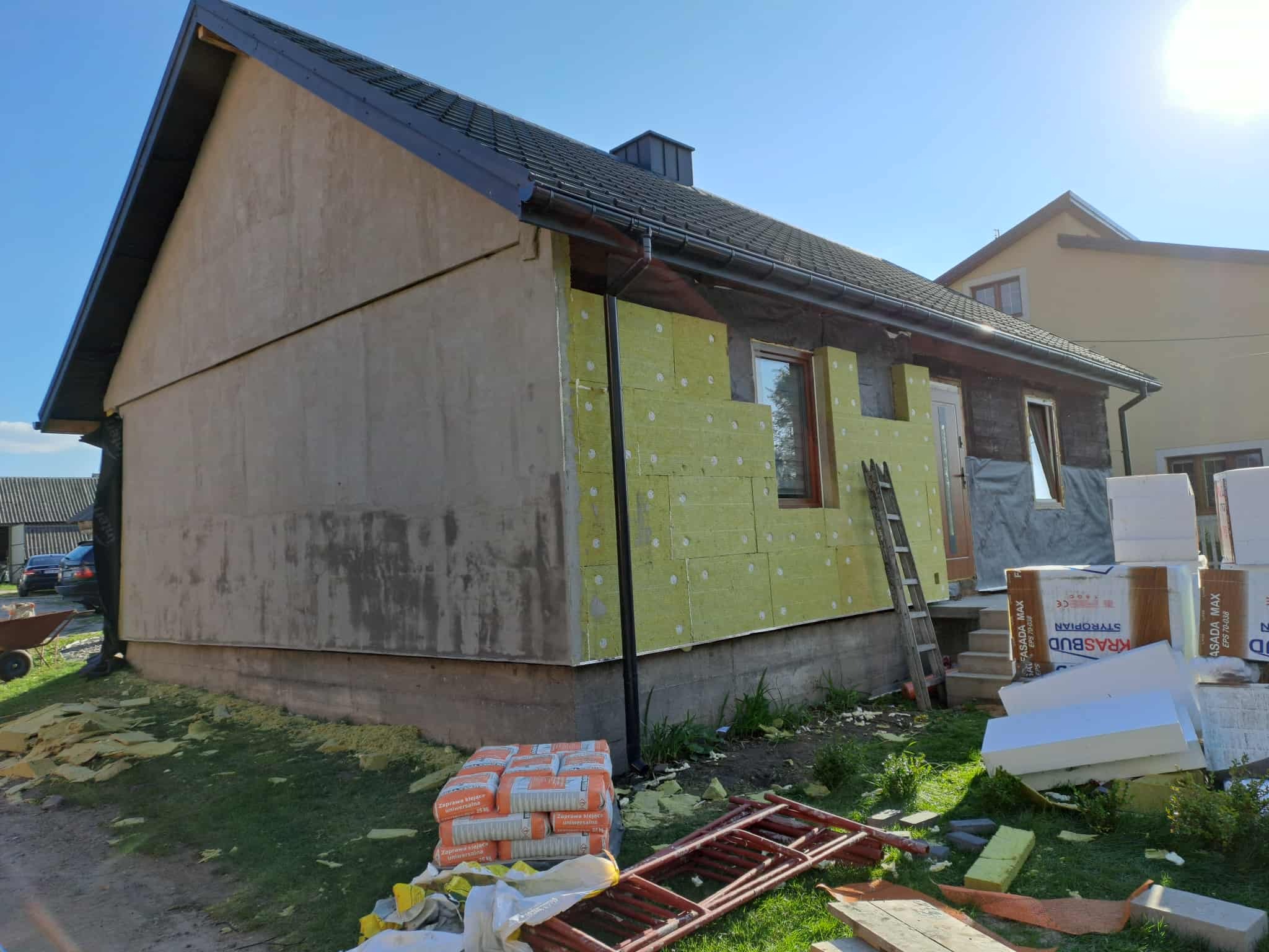 Dom w trakcie ocieplania: fragment elewacji z żółtą wełną mineralną, styropian i zaprawa klejąca obok. Część ściany jeszcze bez ocieplenia.