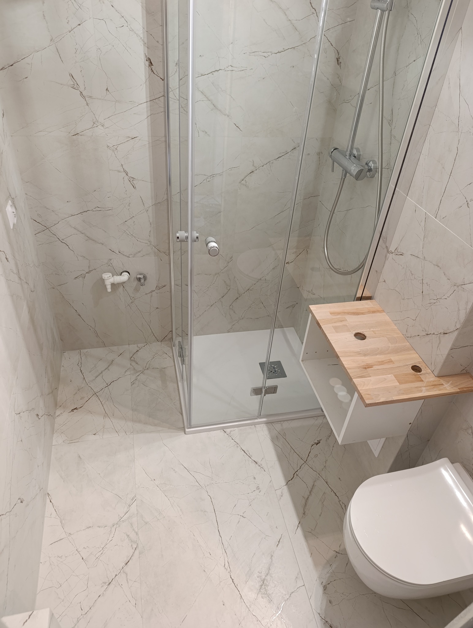 Jasna łazienka z kabiną prysznicową, toaletą i blatem z drewna. Marmurowe płytki na ścianach i podłodze. Nowoczesne wykończenie.