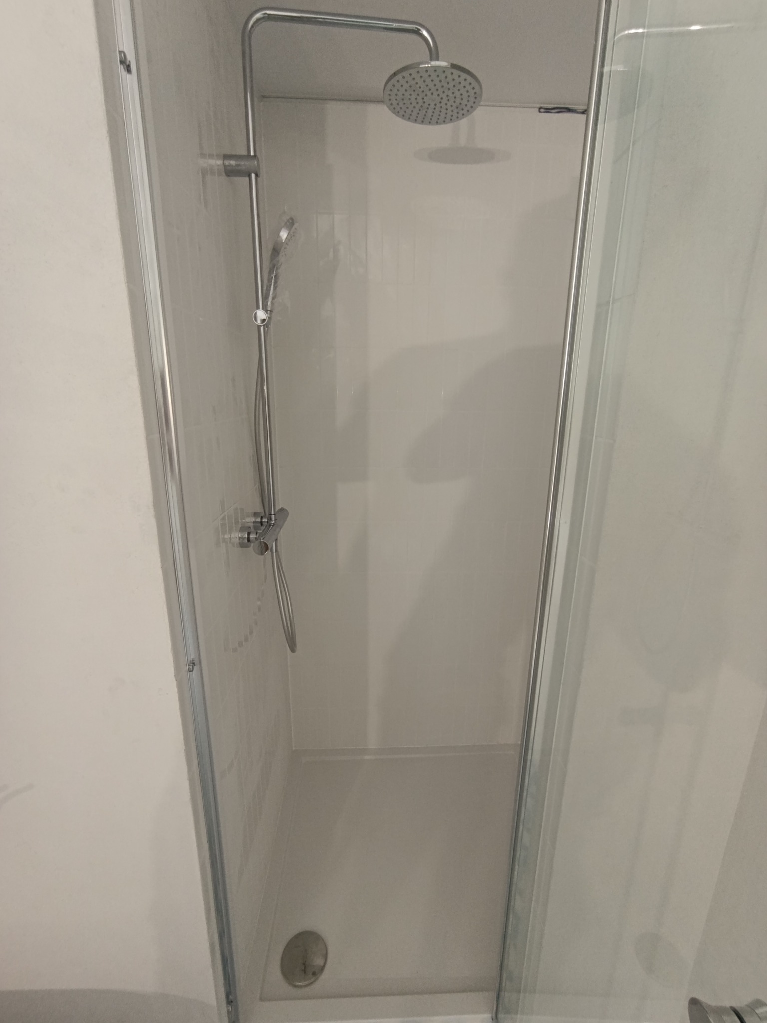 Nowoczesna kabina prysznicowa z deszczownicą i szklanymi drzwiami, wykończona w jasnych odcieniach szarości i bieli, z widocznym odpływem liniowym.