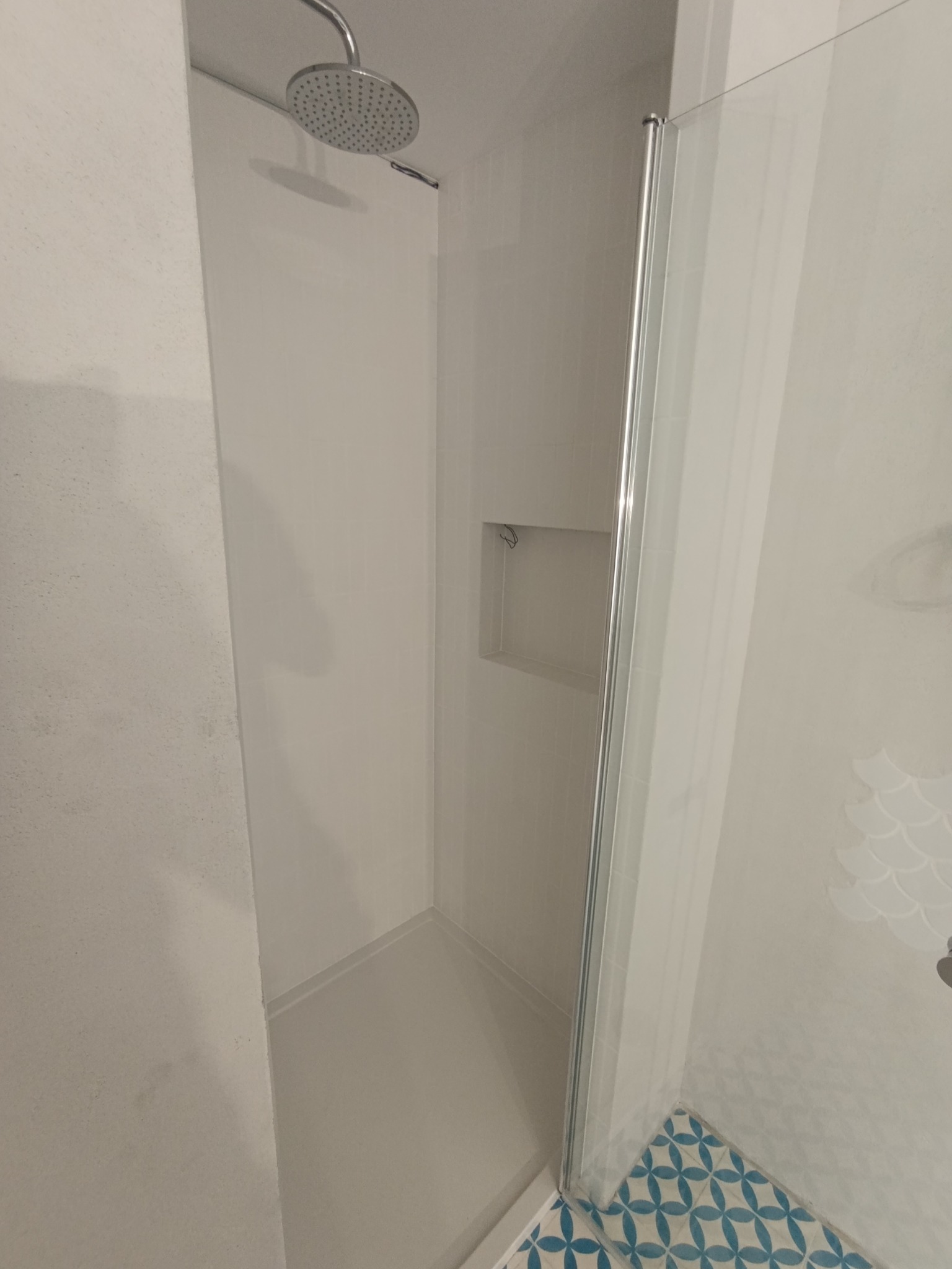 Nowoczesna kabina prysznicowa walk-in z niebieską mozaiką podłogową w Warszawie. Minimalistyczny design z półką w ścianie i deszczownicą.