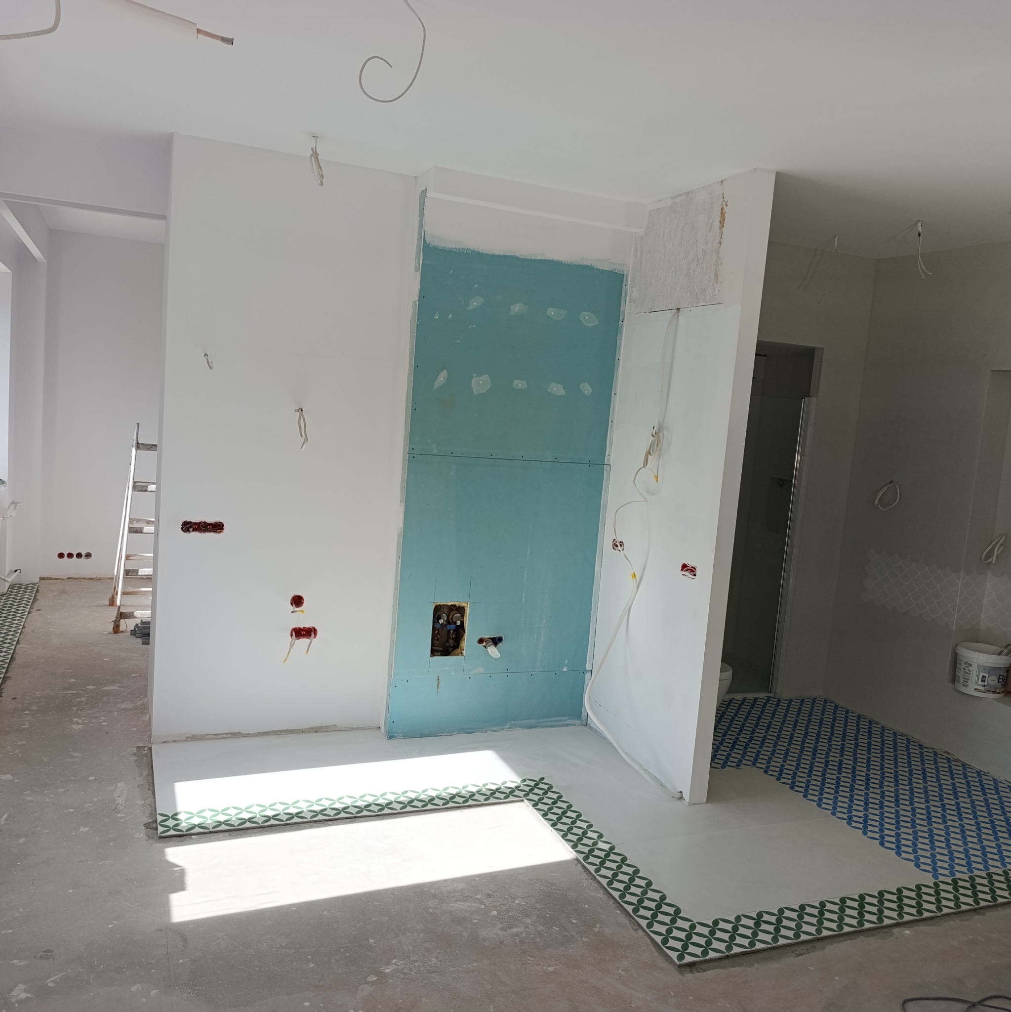 Wnętrze łazienki w trakcie remontu: częściowo ułożone płytki podłogowe z wzorem, ściany przygotowane do dalszych prac, widoczne instalacje.