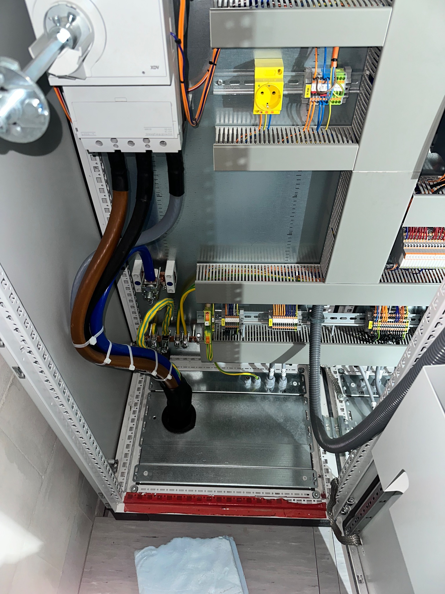 Szafa sterownicza z widocznymi przewodami, złączkami i elementami montażowymi. Przewody prowadzone w peszlach i mocowane opaskami. Widoczne gniazdo i listwy zaciskowe.