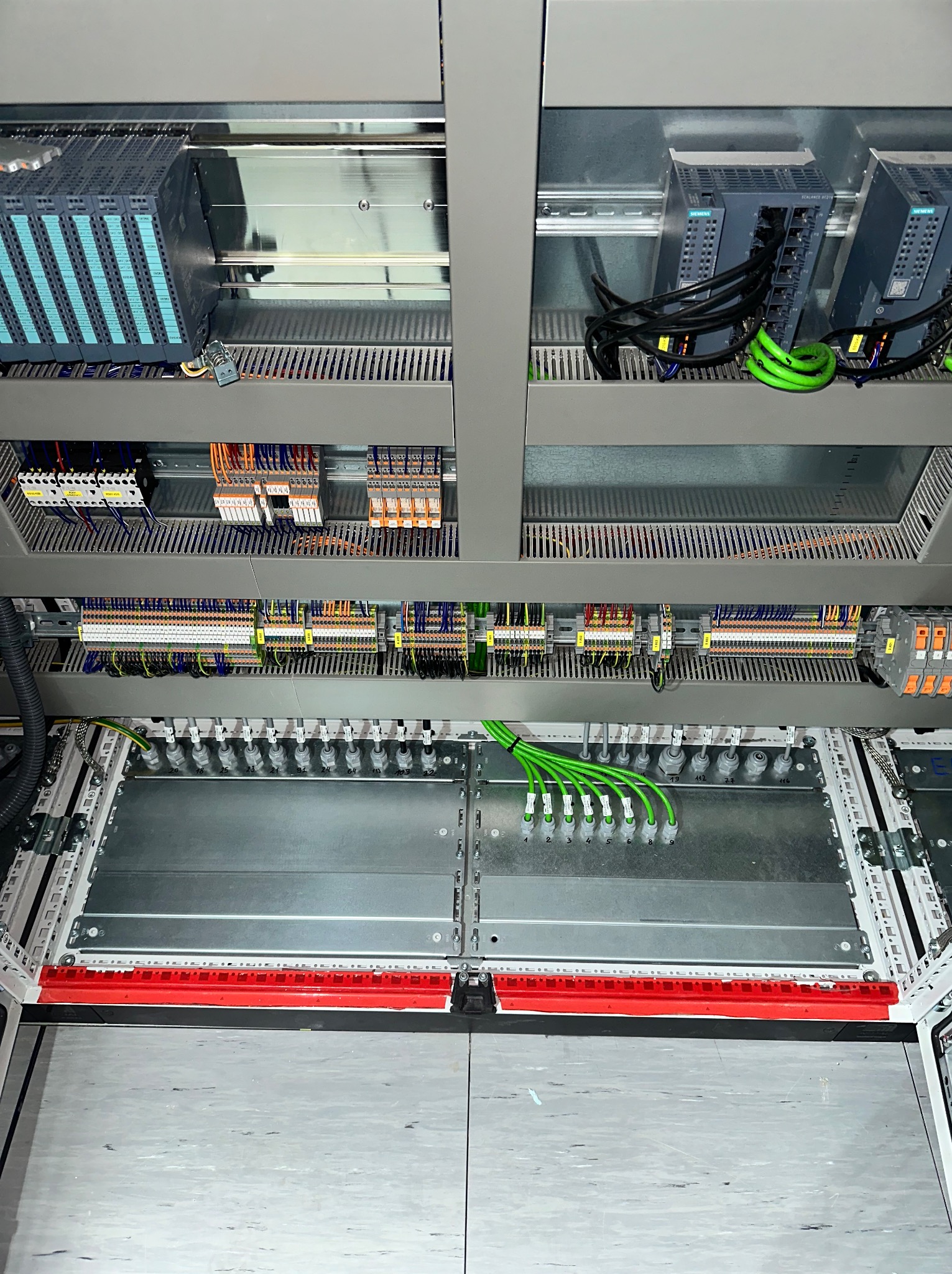 Otwarta szafa sterownicza z modułami Siemens, okablowaniem i listwami zaciskowymi. Widoczne przewody w kolorach, w tym charakterystyczne zielone.