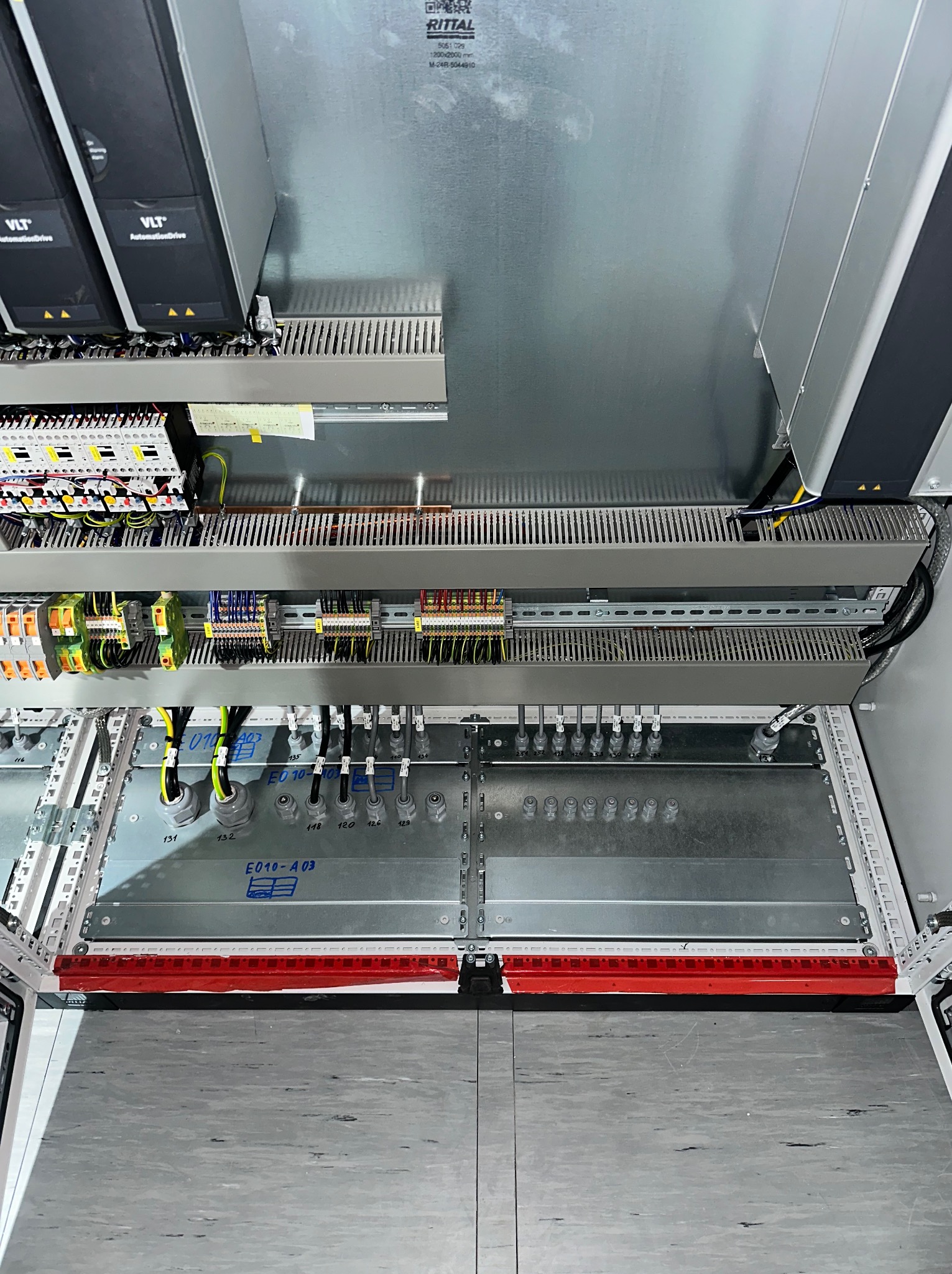 Wnętrze szafy sterowniczej Rittal z modułami VLT AutomationDrive, okablowaniem i elementami montażowymi. Widok z góry na rozdzielnicę elektryczną.