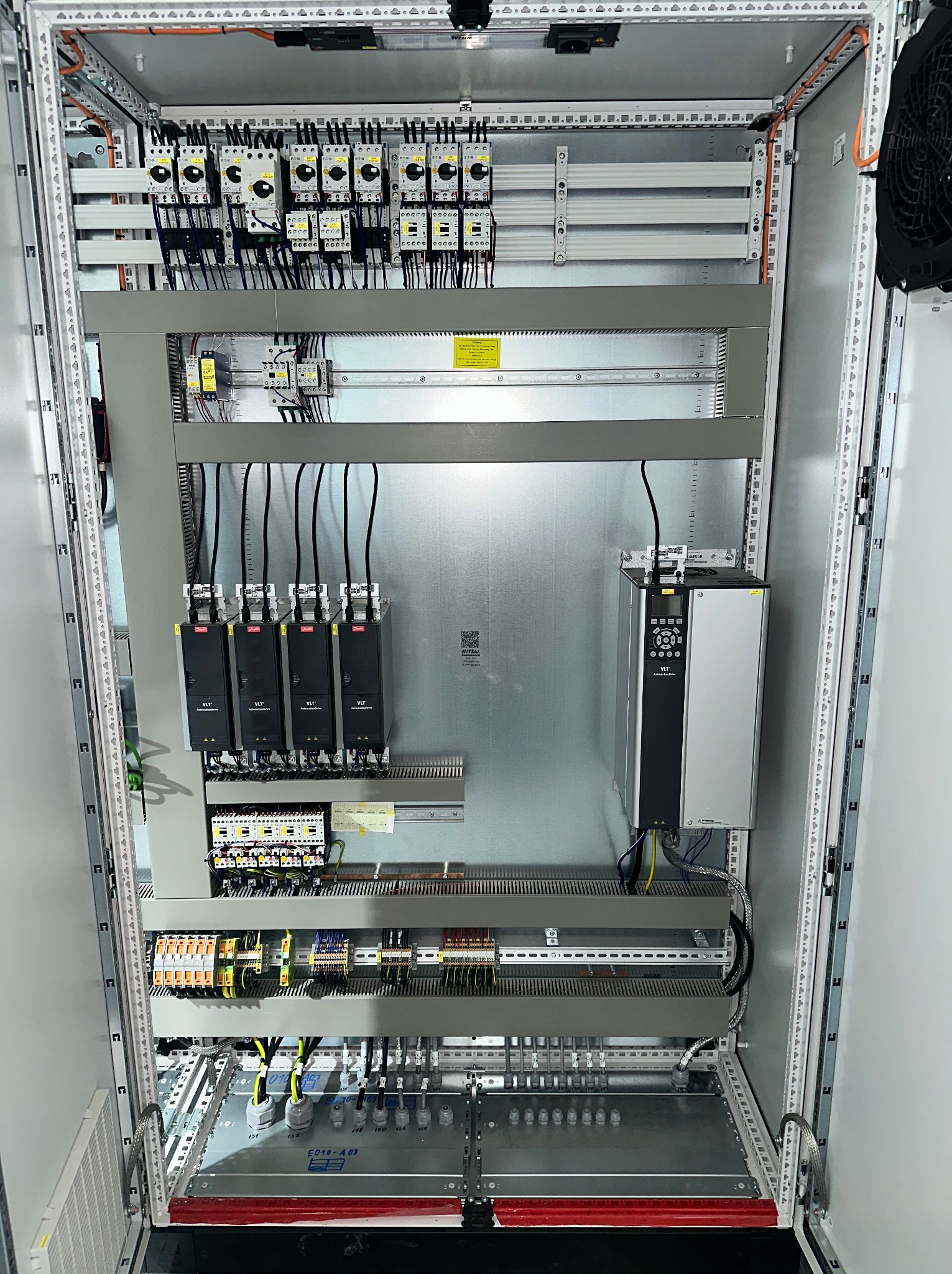 Szafa sterownicza z zamontowanymi elementami elektrycznymi, w tym przekaźniki, zasilacze i sterowniki VLT. Widoczne przewody i listwy montażowe wewnątrz obudowy.