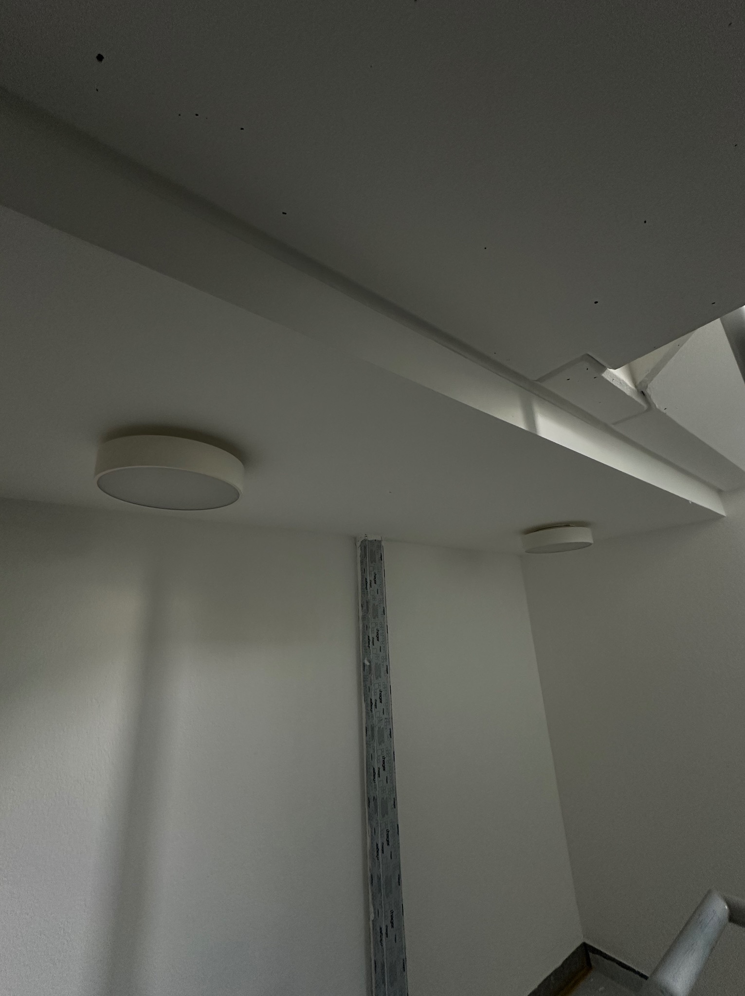 Zamontowane okrągłe lampy sufitowe w białym pomieszczeniu, widoczne szyny montażowe na ścianie. Minimalistyczny design, świeże, jasne wnętrze.