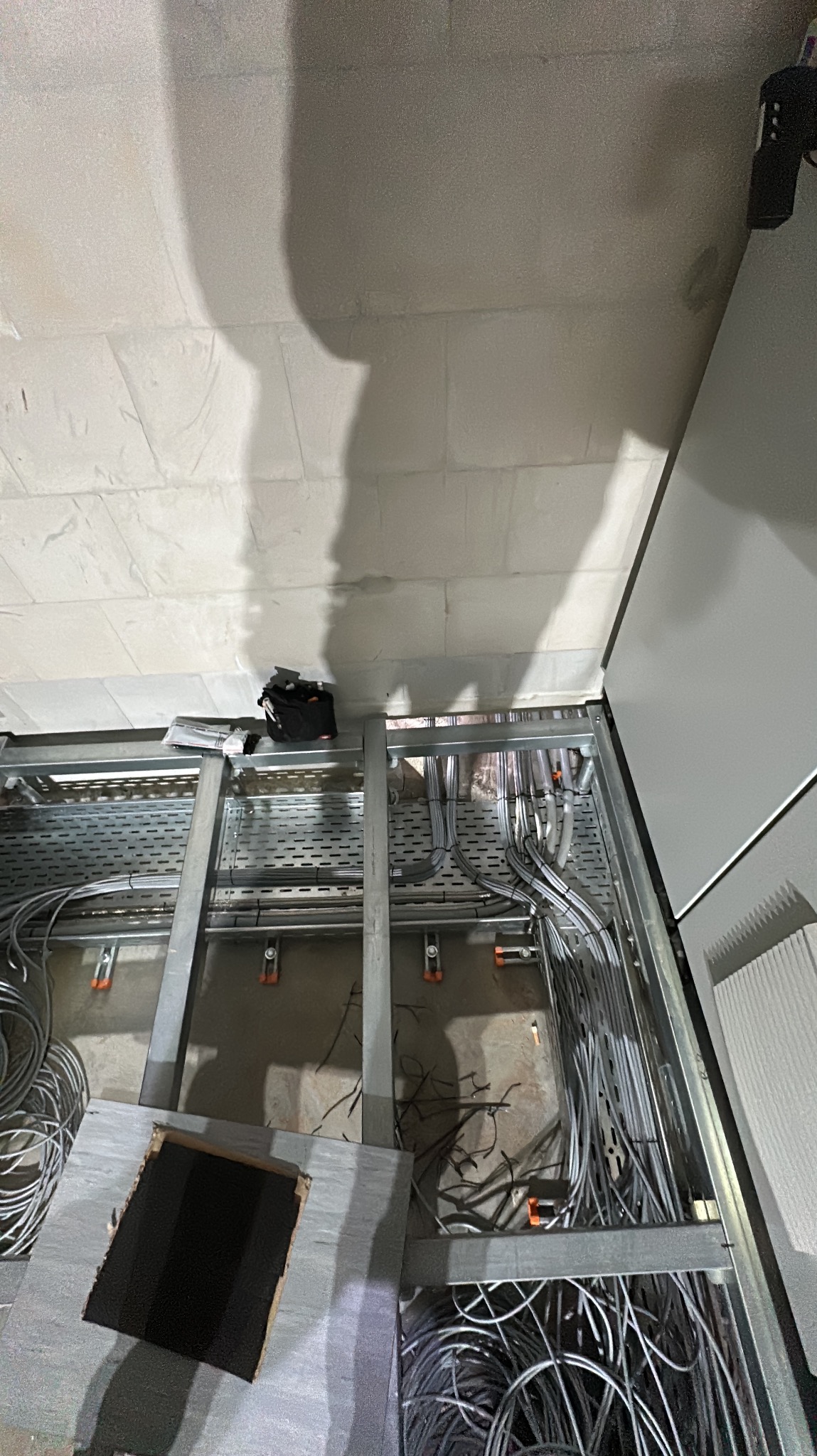 Metalowa konstrukcja pod podłogą techniczną z ułożonymi kablami elektrycznymi; torba narzędziowa na konstrukcji, widok z góry, surowy betonowy strop.