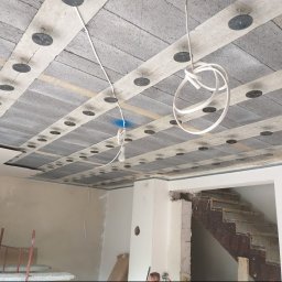 Fach-Mal - Montaż sufitu z betonowych paneli z widocznymi elementami mocującymi. Przewody elektryczne zwisają z sufitu. W tle widoczne schody w trakcie remontu.