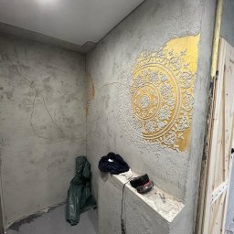 Fach-Mal - Wykończenie ścian z dekoracyjnym, wypukłym wzorem mandali na złotej farbie. Widoczne narzędzia i ubrania robocze, wnętrze w trakcie prac wykończeniowych.