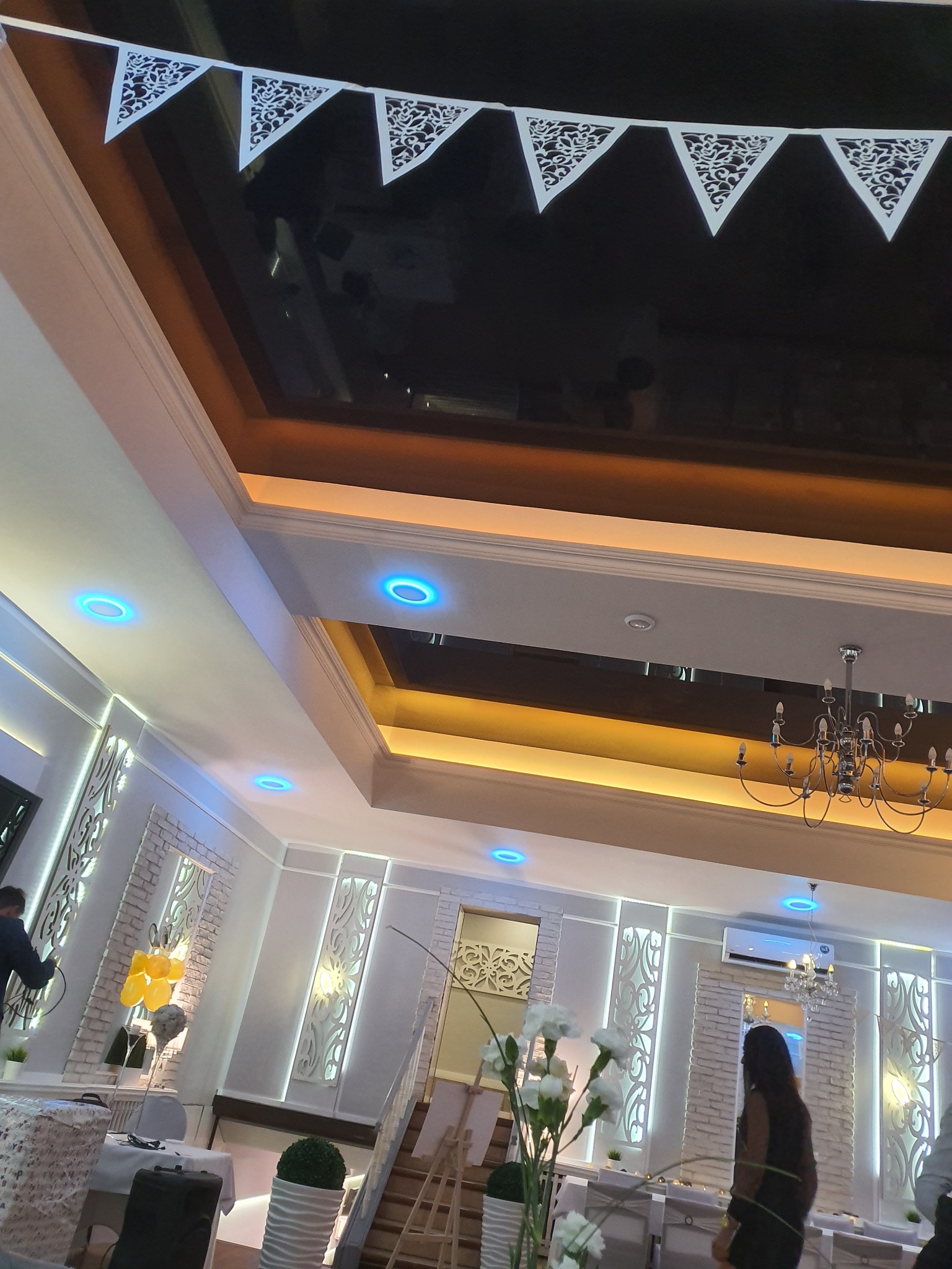 Eleganckie wnętrze sali bankietowej z dekoracjami: girlanda, żyrandol, podświetlane elementy ścienne i sufitowe. Przygotowania do uroczystości.