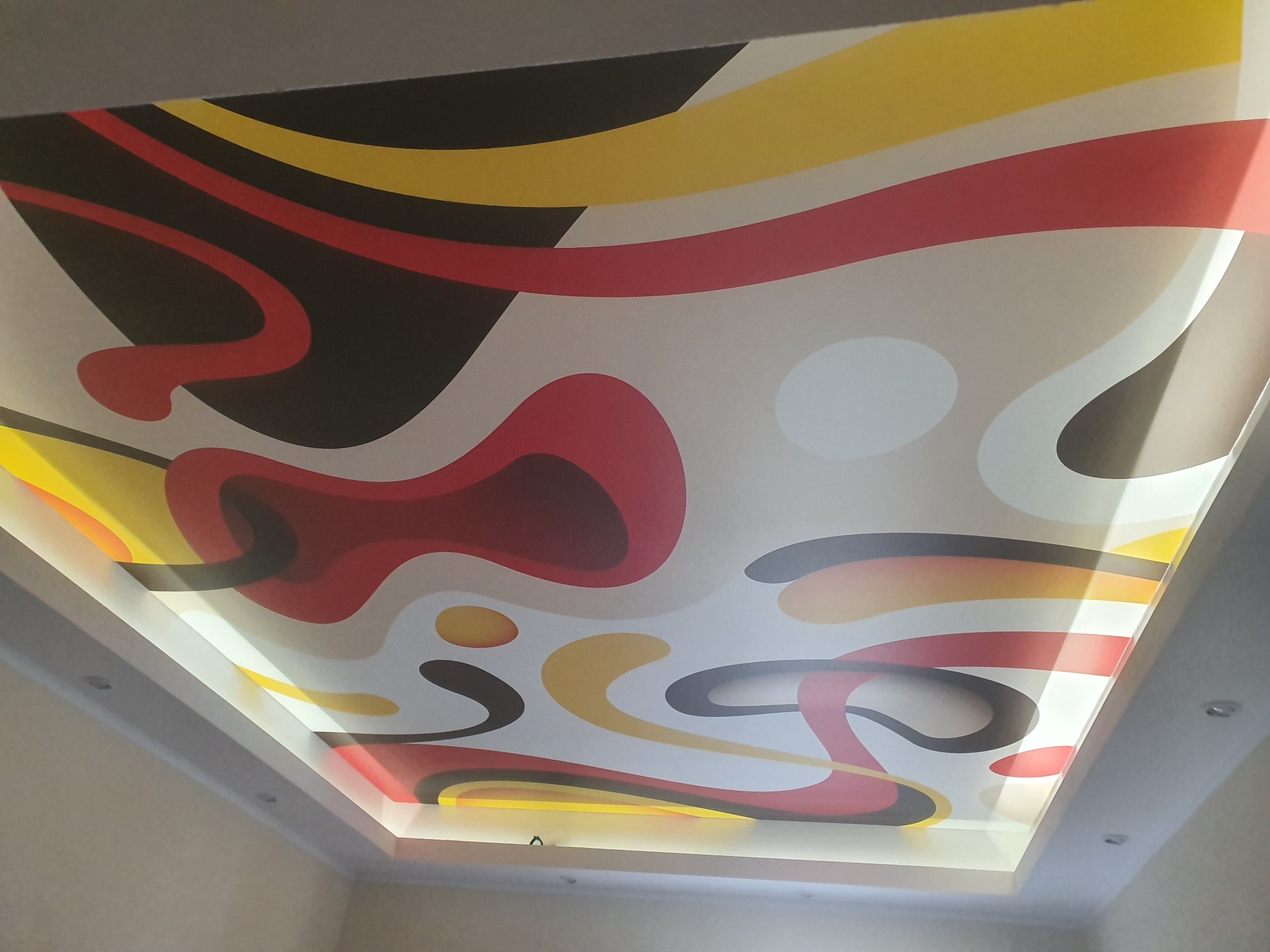 Podświetlany sufit napinany z abstrakcyjnym wzorem w kolorach czerwonym, żółtym i czarnym, oświetlony od spodu, widoczny z perspektywy żabiej.