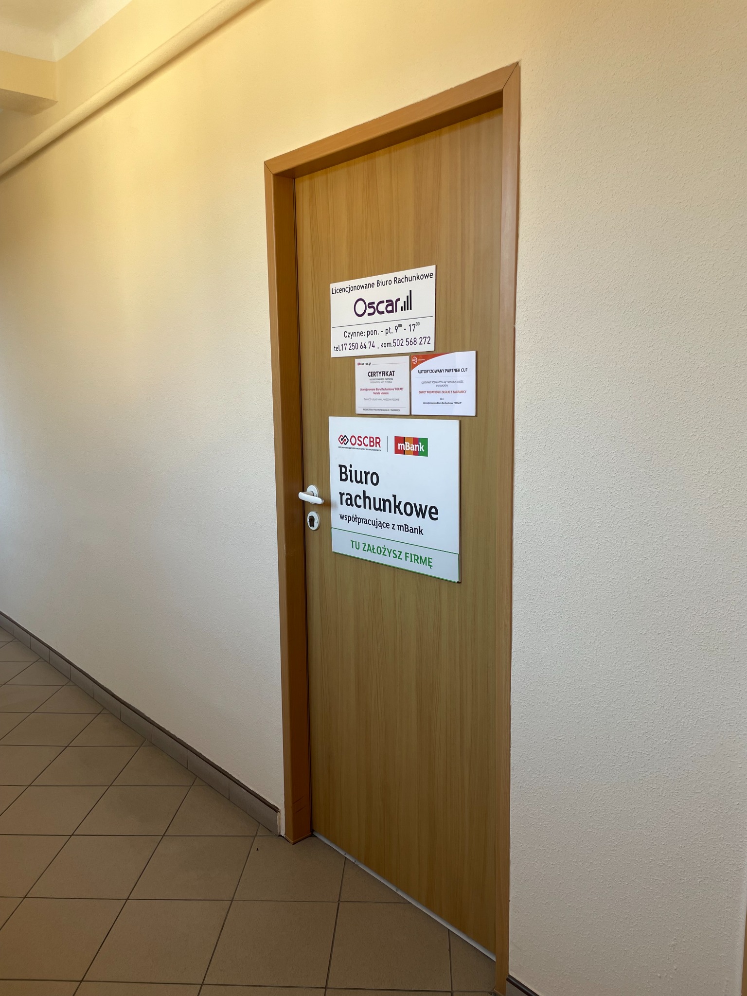 Drzwi do biura rachunkowego Oscar.ill z informacją o godzinach otwarcia, numerach kontaktowych i certyfikatach. Widoczne logo OSCBR i mBank.