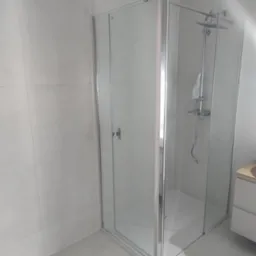 Nowoczesna kabina prysznicowa z chromowanymi profilami i deszczownicą, jasne płytki na ścianach i podłodze, minimalistyczny design.