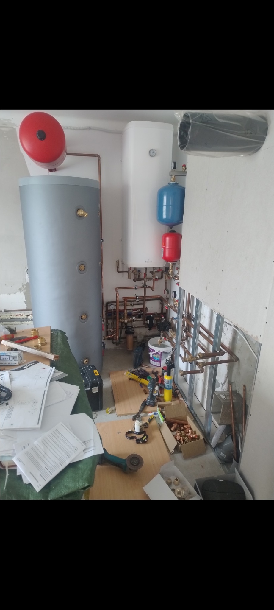 Montaż instalacji CO i CWU w łazience: zbiorniki, rury miedziane, narzędzia. Widoczny etap prac, nieukończone ściany. Instalacja grzewcza w trakcie realizacji.