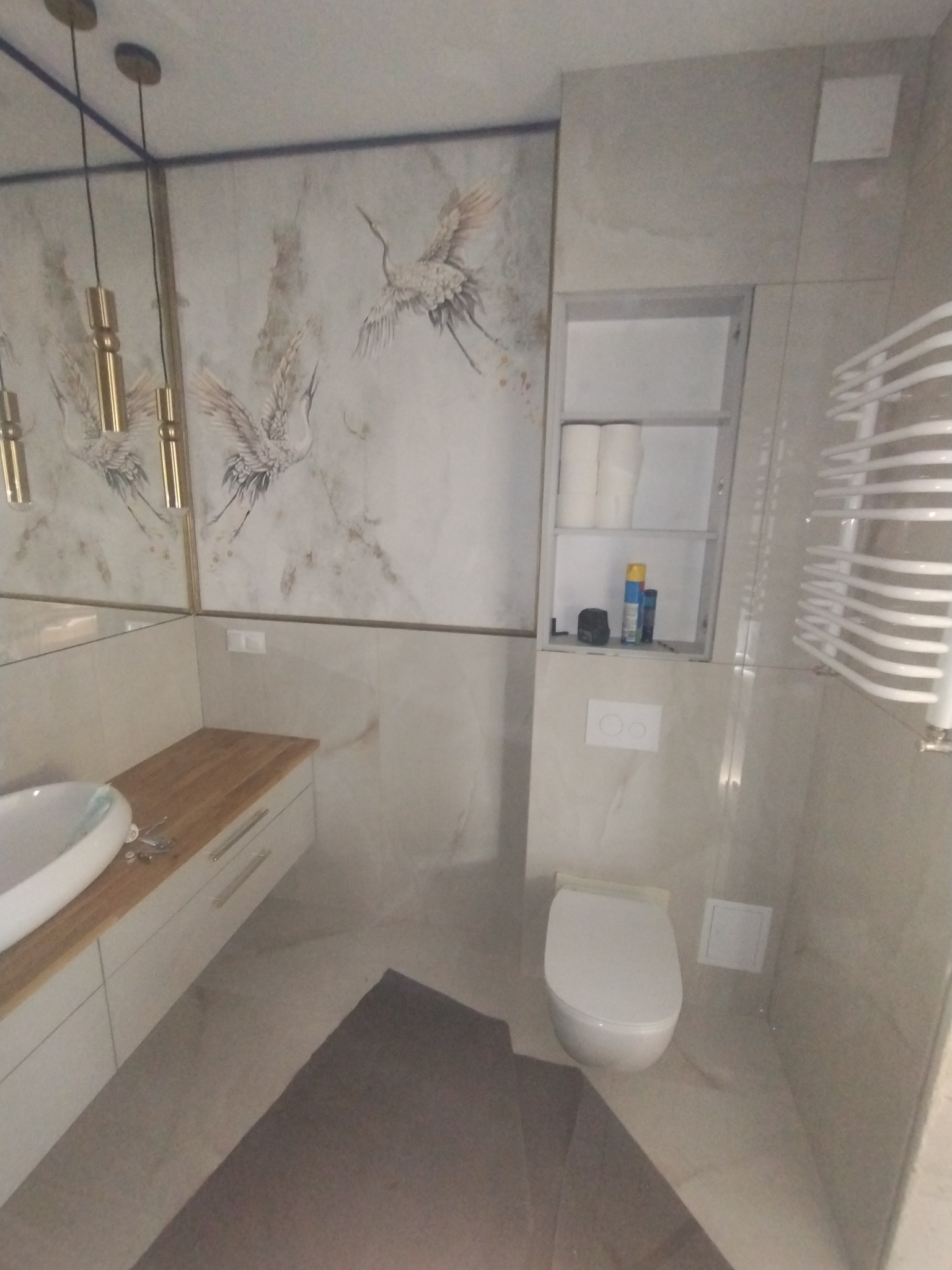 Nowoczesna łazienka z motywem żurawi na ścianie, drewnianym blatem umywalki, zabudowaną szafką i grzejnikiem drabinkowym. Neutralna kolorystyka wnętrza.