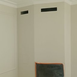 Drewniak Glazurnictwo - Wnętrze po malowaniu: kremowe ściany z dekoracyjną sztukaterią, zabezpieczony kominek i otwory wentylacyjne. Podłoga zakryta folią ochronną. Widok na wykończony róg pomieszczenia.