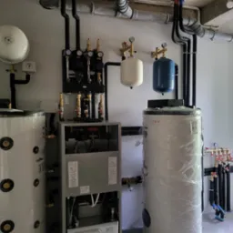 Złożony system grzewczy z dwoma zbiornikami, rozdzielaczami i pompami, instalacja hydrauliczna z rurami i zaworami.