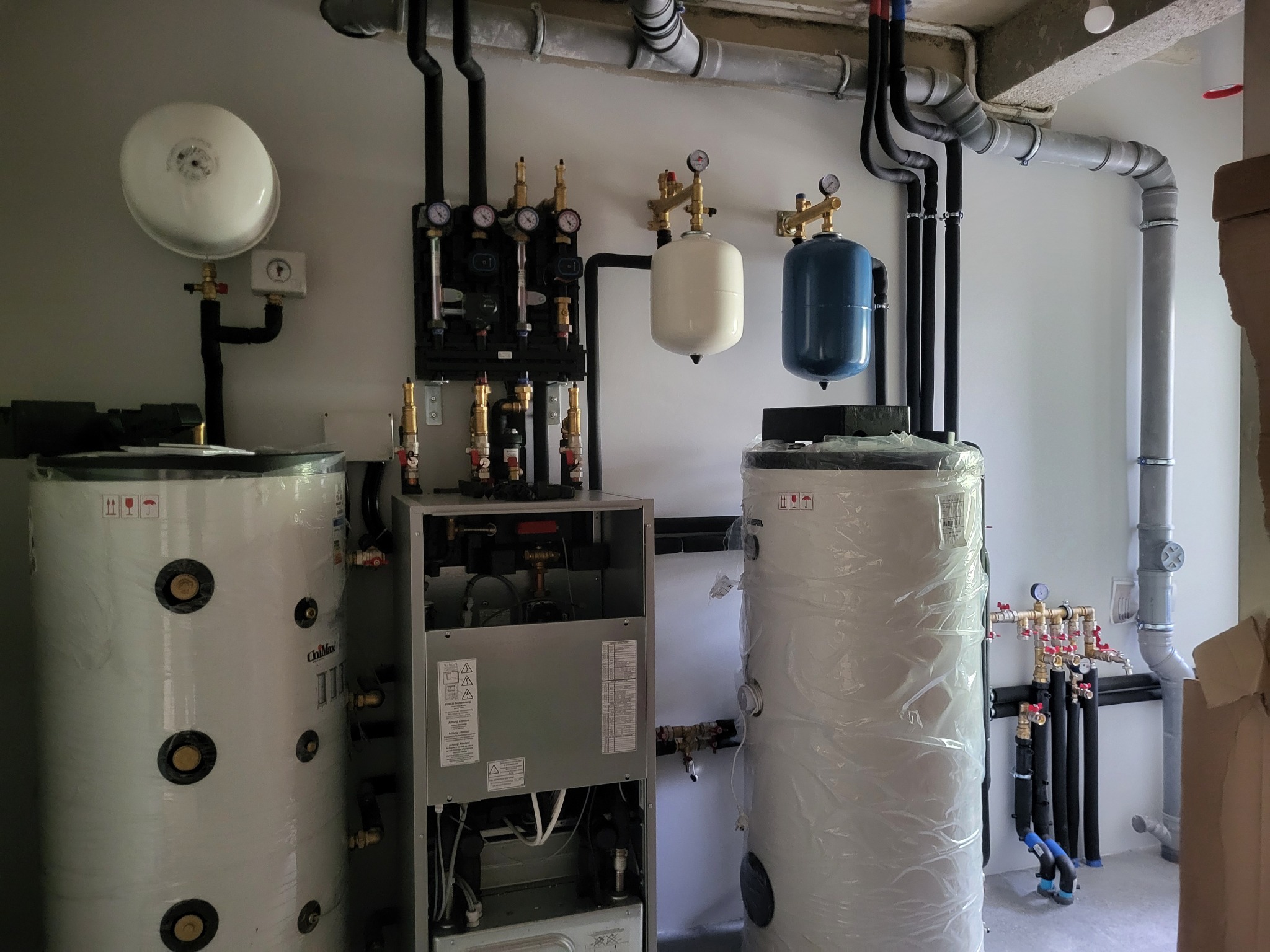 Złożony system grzewczy z dwoma zbiornikami, rozdzielaczami i pompami, instalacja hydrauliczna z rurami i zaworami.