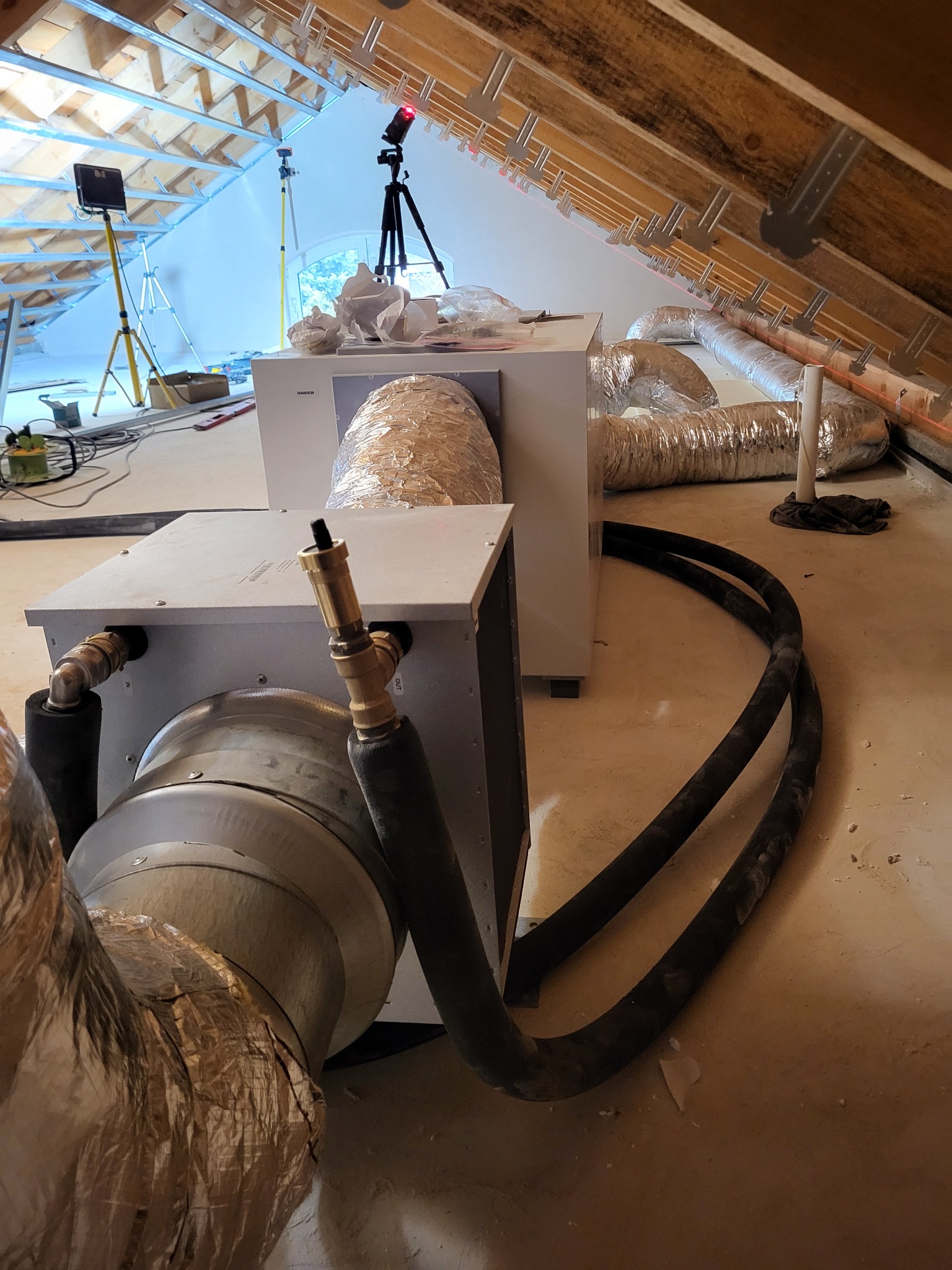 Instalacja rekuperacji w surowym wnętrzu poddasza z widocznymi elementami izolacji i przewodami wentylacyjnymi. Widoczny laser krzyżowy.