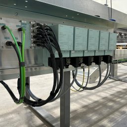 EKSS Jakub Klimontowicz - Panel sterowania Siemens z licznymi kablami i złączami, zamontowany na metalowej konstrukcji. Widoczne moduły sterujące i okablowanie w kolorach czarnym, szarym i zielonym.