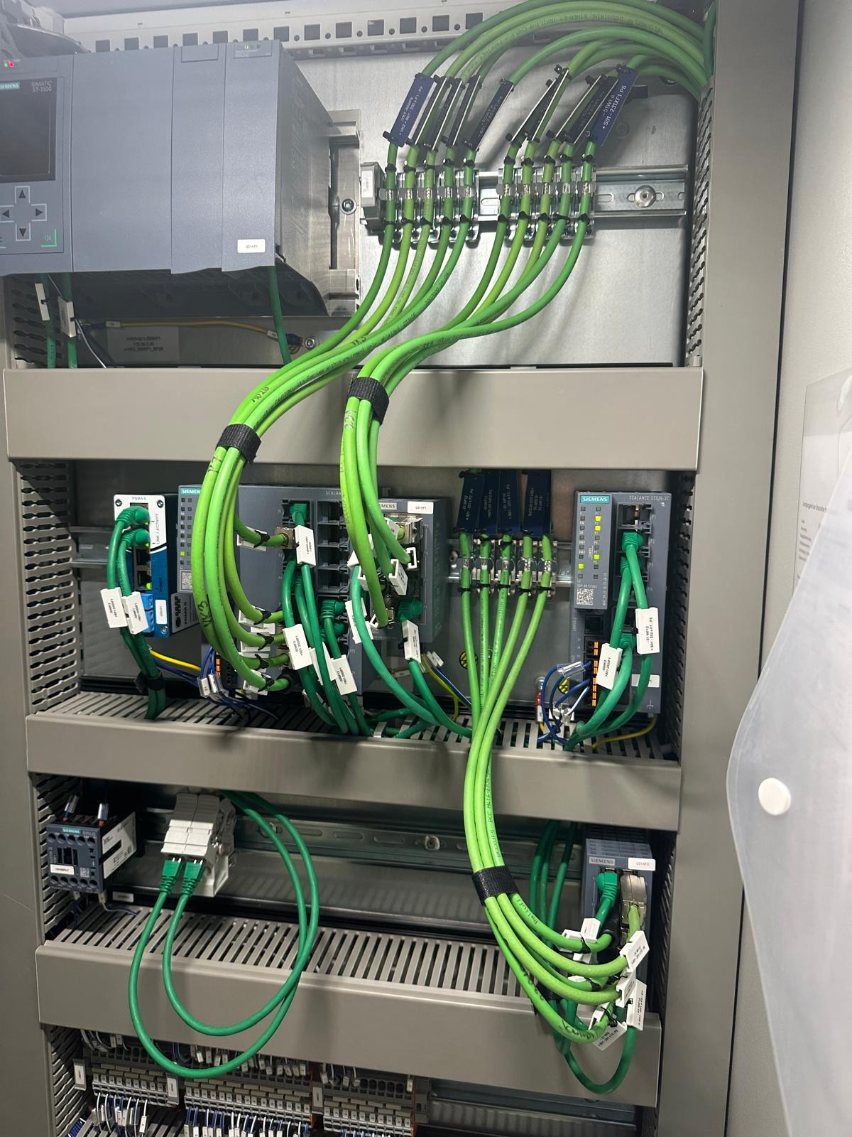 Panel sterowniczy z precyzyjnie ułożonymi, zielonymi kablami Ethernet, uporządkowanymi za pomocą rzepów i podłączonymi do modułów Siemens. Widoczne oznaczenia na kablach.