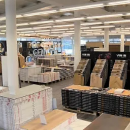 Szeroki kadr na ekspozycję paneli i drzwi w przestronnym salonie z jasnym oświetleniem. Widoczne wzorniki i opakowania produktów.