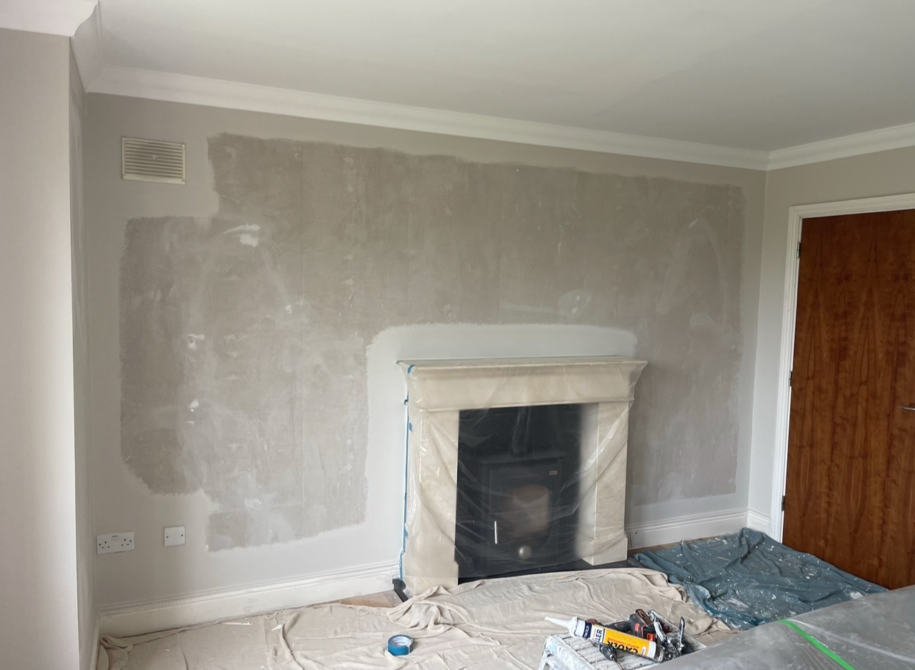 Ściana po szpachlowaniu, przygotowana do malowania. Kominek zabezpieczony folią, podłoga przykryta plandeką. Widoczne narzędzia pracy.