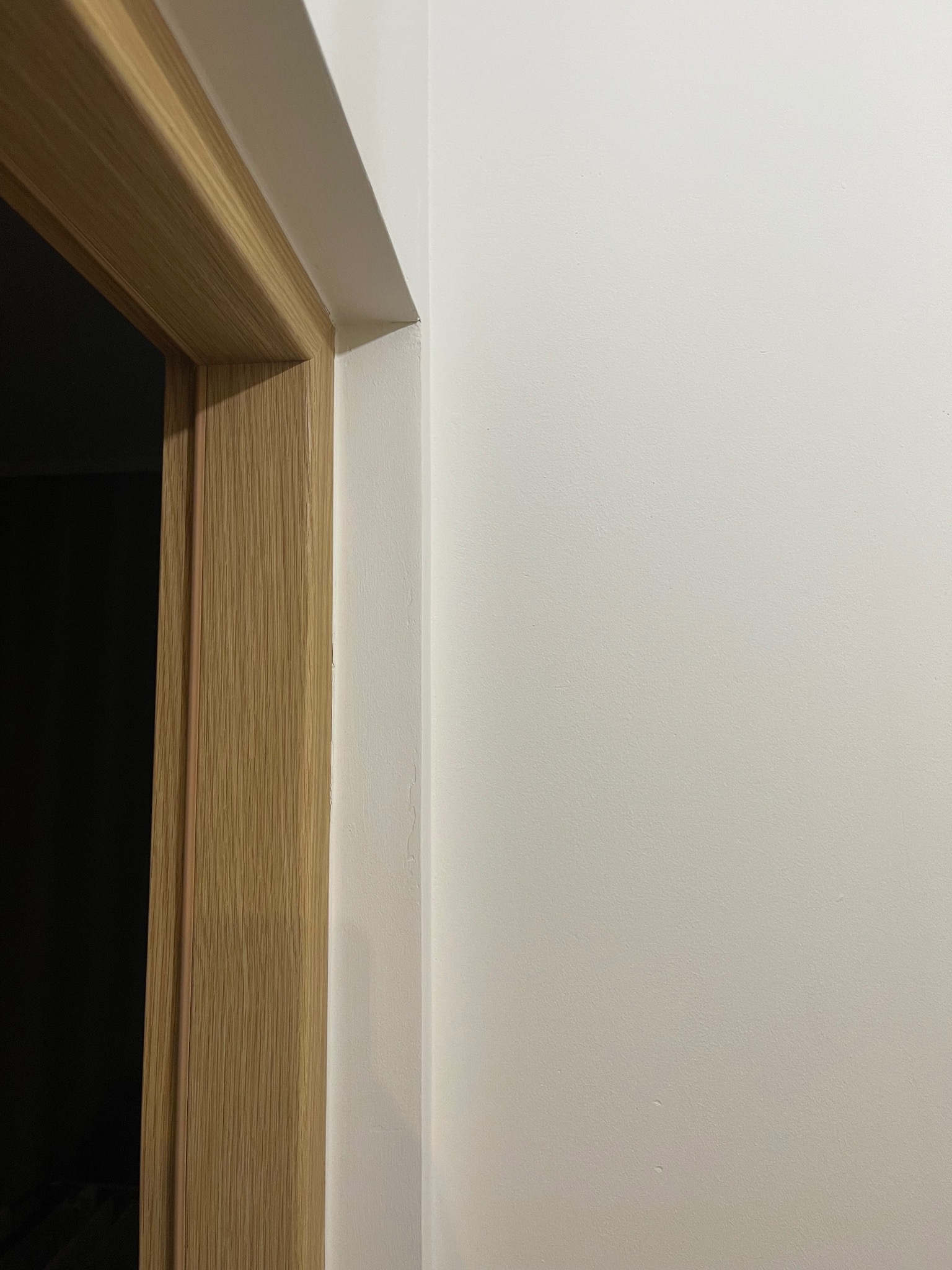 Gładka, biała ściana po malowaniu z widoczną ościeżnicą drzwiową z jasnego drewna. Fragment wykończonego wnętrza, minimalistyczny styl.