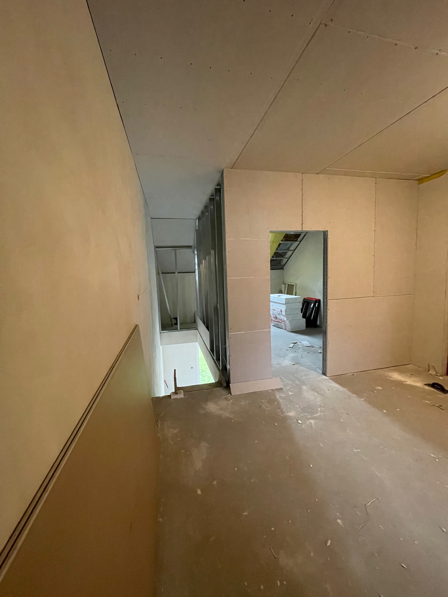 Wnętrze w trakcie montażu płyt kartonowo-gipsowych na ścianach i suficie. Widoczne metalowe profile konstrukcyjne i przygotowane wejście do innego pomieszczenia.