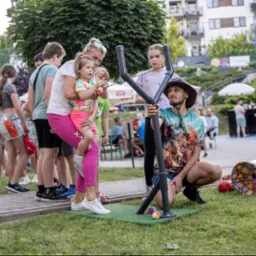 Impreza plenerowa w Przemyślu: animator z dziećmi celują z dużej procy do celu. W tle widoczni inni uczestnicy zabawy i budynki mieszkalne.