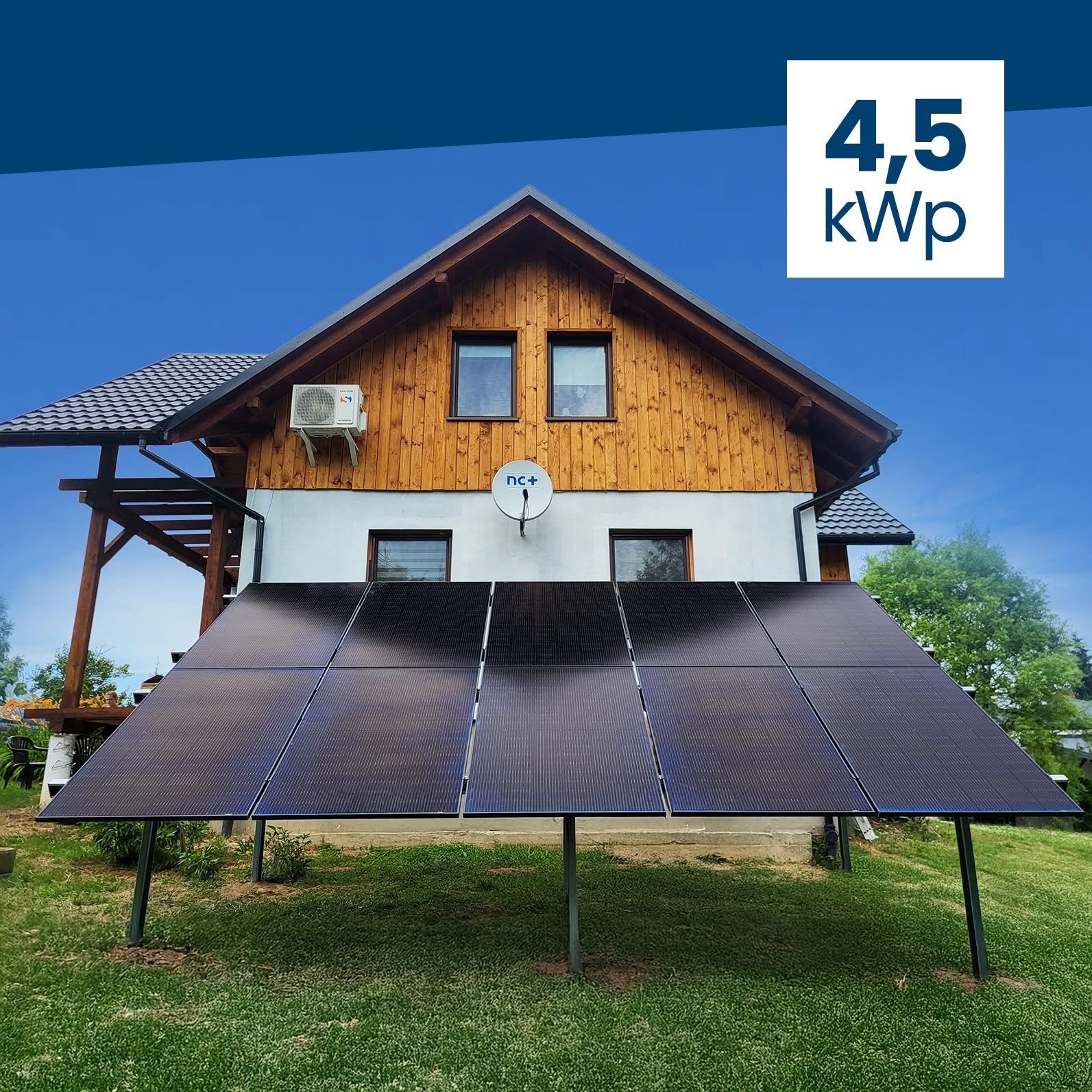 Panele fotowoltaiczne 4,5 kWp na trawniku przed domem z drewnianą elewacją. Widoczny klimatyzator i antena satelitarna na ścianie budynku. Błękitne niebo w tle.