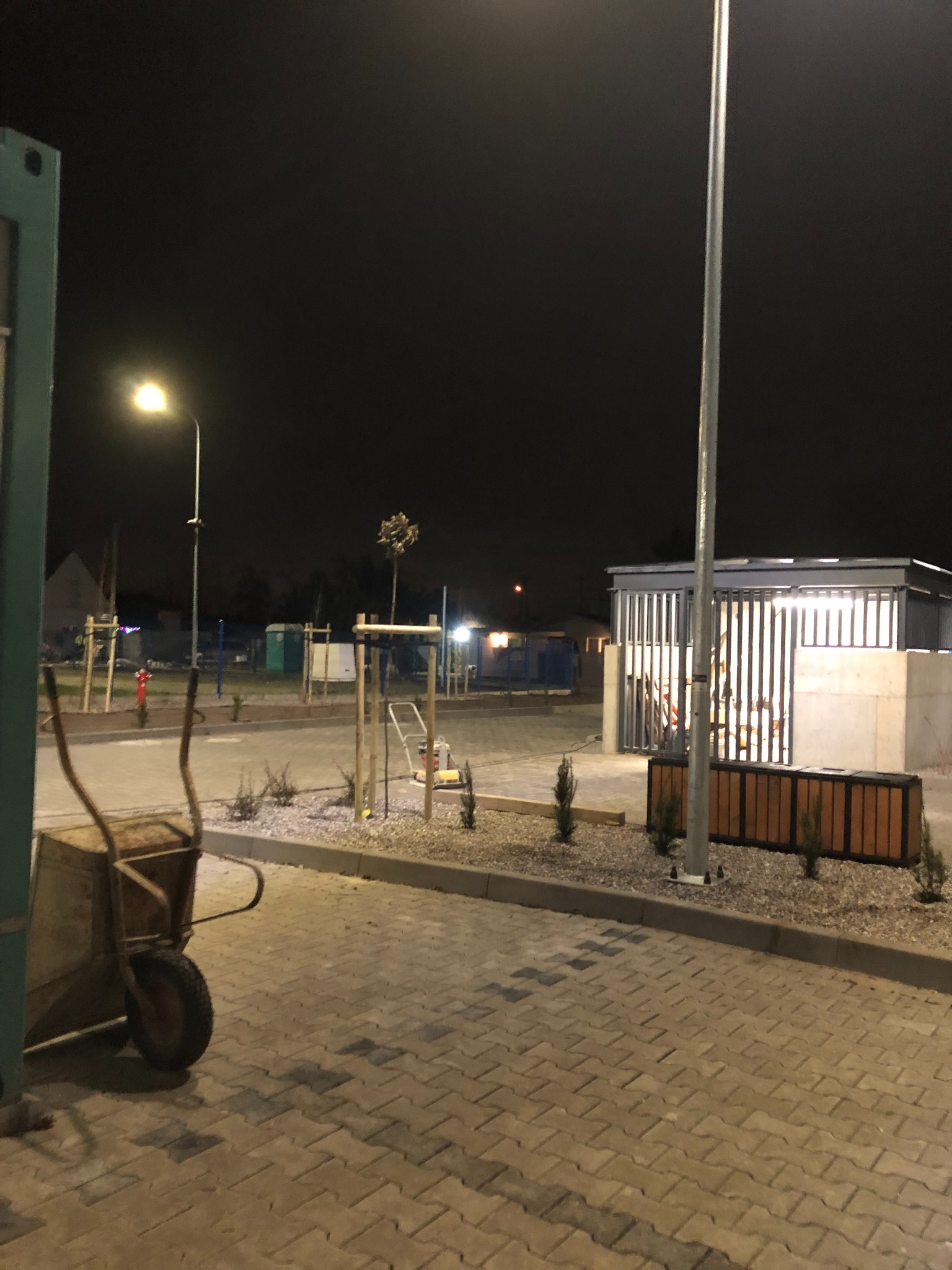 Nocne układanie kostki brukowej w Szamotułach. W tle widoczny postęp prac i oświetlenie uliczne, a na pierwszym planie taczka.