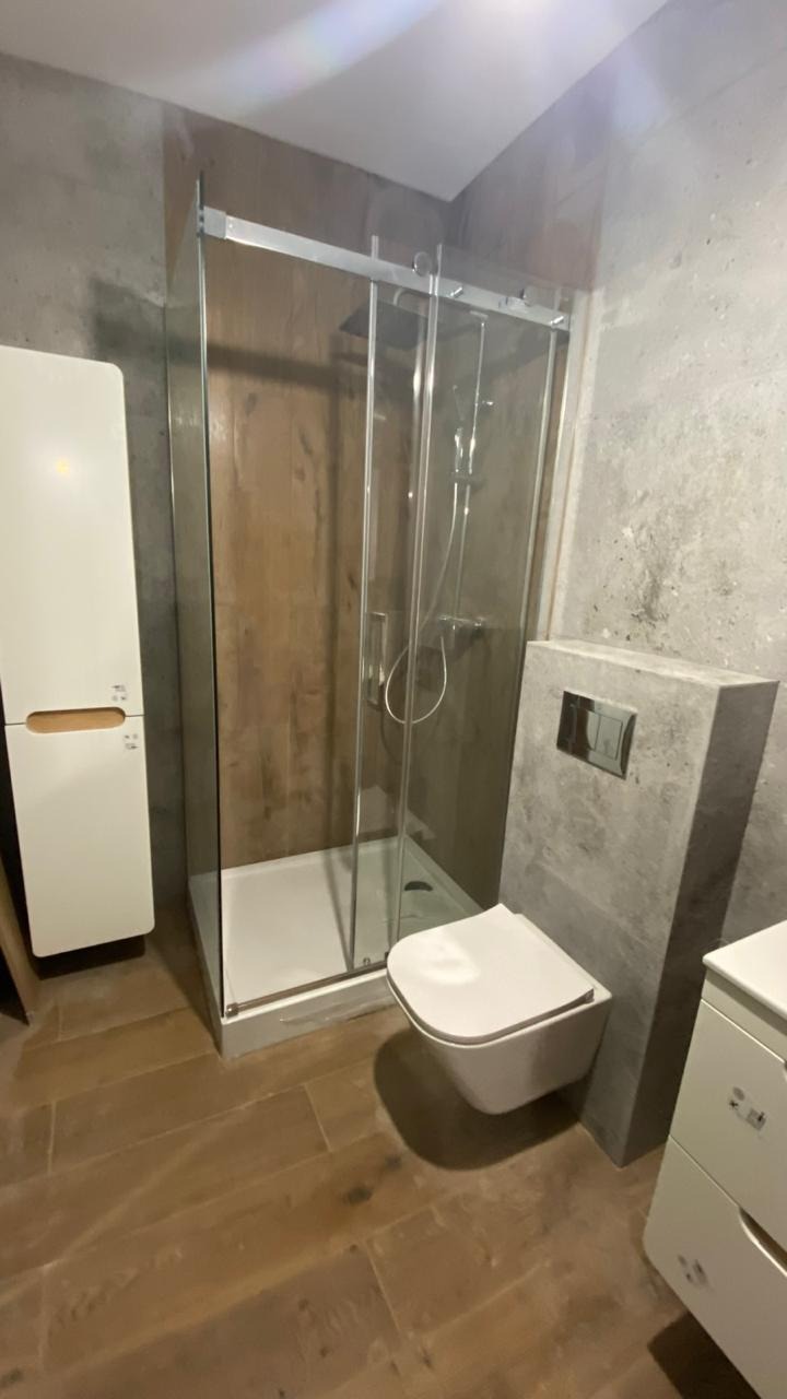 Nowoczesna łazienka z kabiną prysznicową, podwieszaną toaletą i drewnopodobną podłogą. Ściany w odcieniach szarości. Minimalistyczny design.