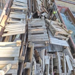 MultiWork Bartosz Pietrzyk - Kontener wypełniony starymi, drewnianymi paletami i fragmentami desek po rozbiórce, z widocznym fragmentem buta osoby stojącej obok.