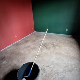 MultiWork Bartosz Pietrzyk - Pokój po malowaniu ścian na czerwono i zielono, z wałkiem do malowania w wiadrze. Podłoga zabezpieczona folią malarską. Widok na odświeżone wnętrze.