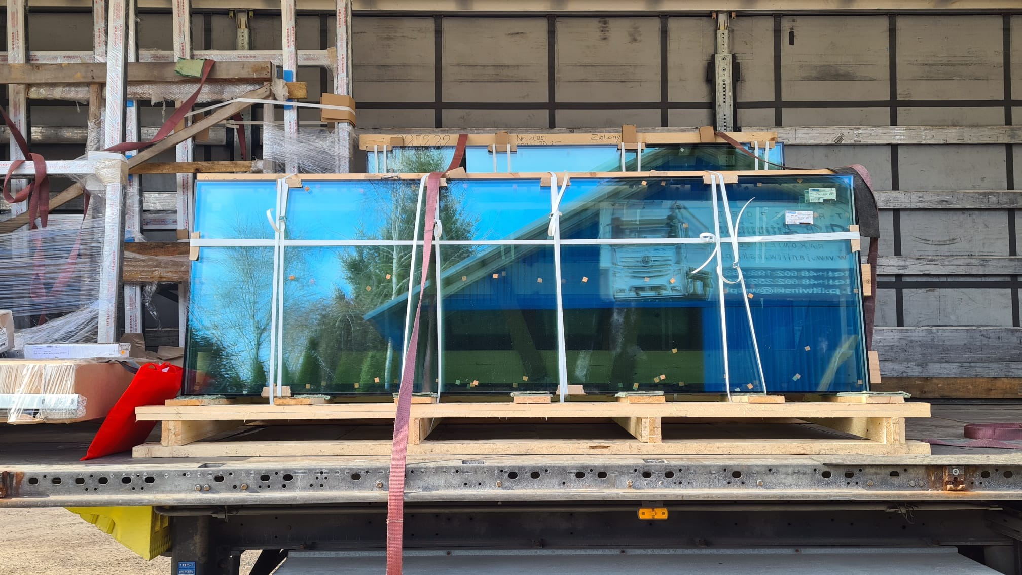 Transport okien: szyby okienne zabezpieczone na paletach wewnątrz ciężarówki, gotowe do przewozu. Widoczne detale mocowania i odblask otoczenia w szkle.